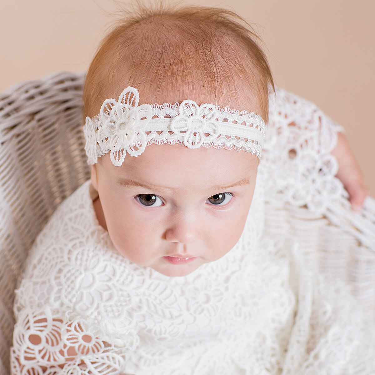 Baby wearing a white lace headband and blanket on a beige background