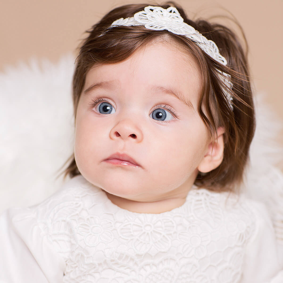 Baby with a white headband and white outfit lying on a soft surface
