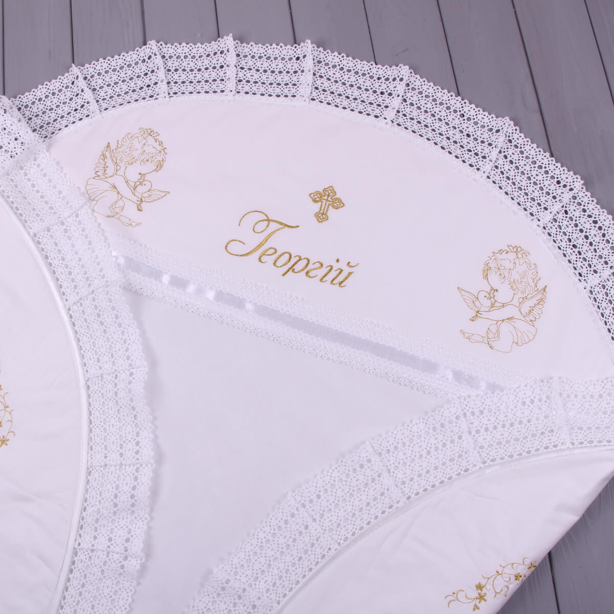 White embroidered baby blanket with gold designs on a wooden surface