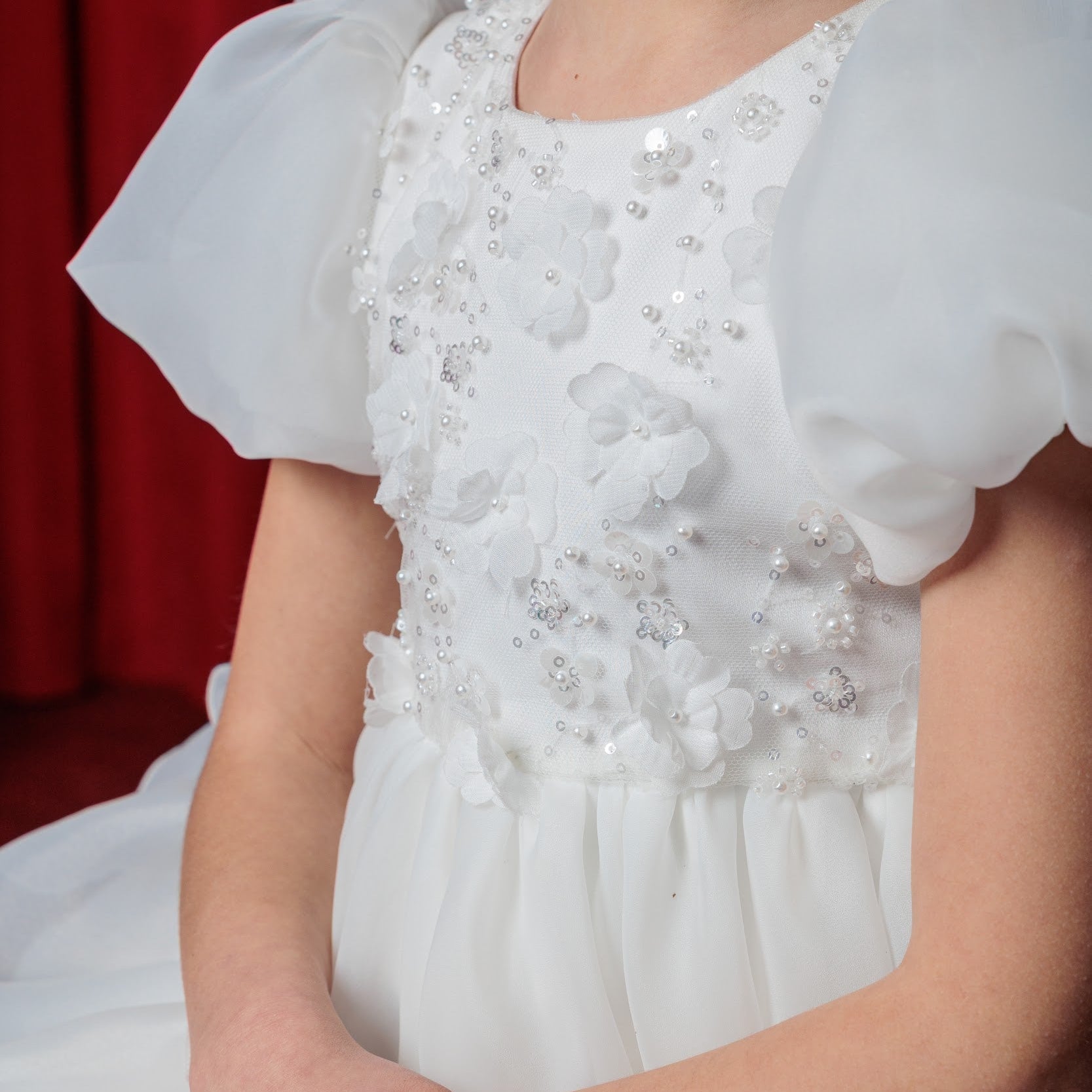 White dress with ruffled sleeves worn by a person against a red curtain background