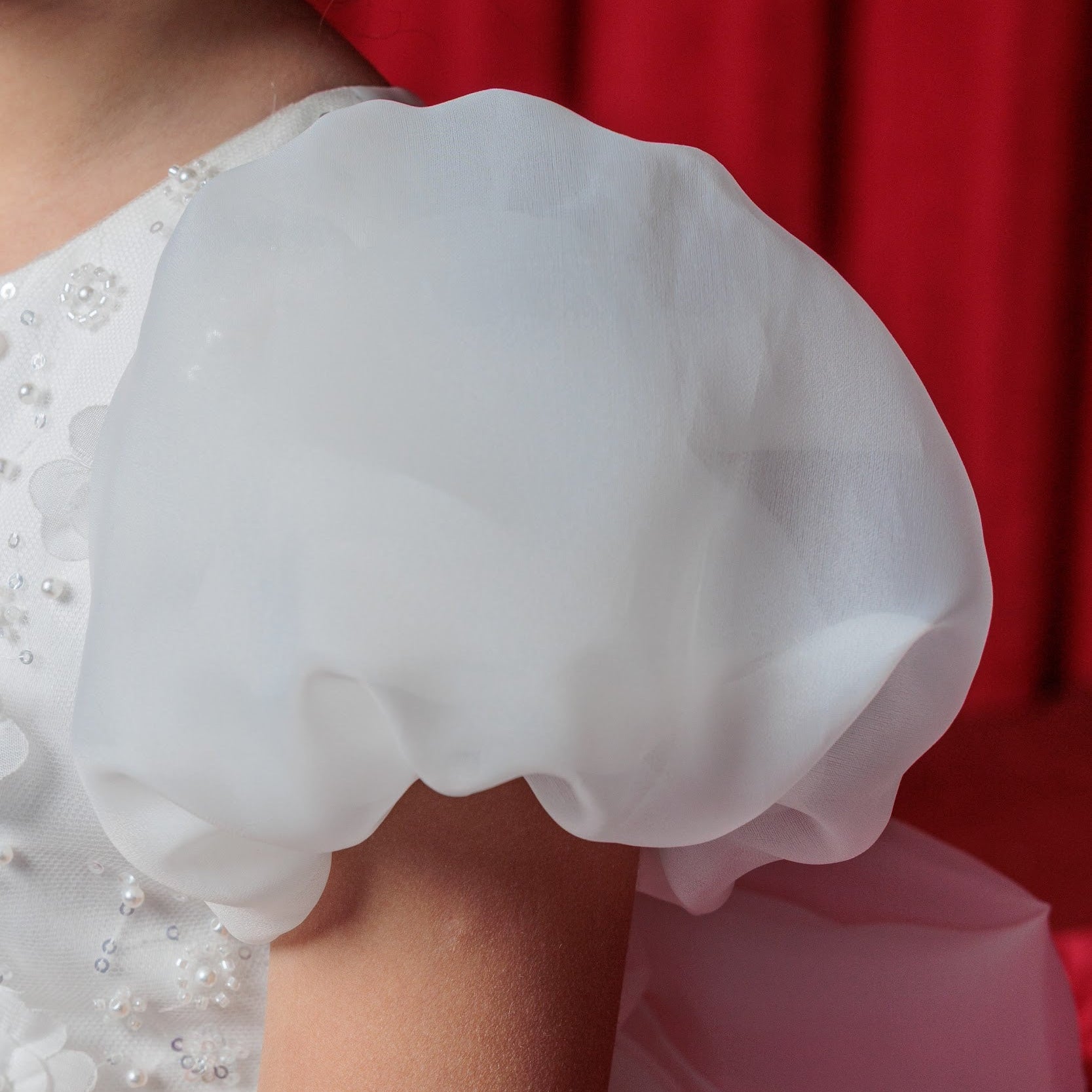Close-up of a white lace sleeve on a person wearing a wedding dress with a red background.