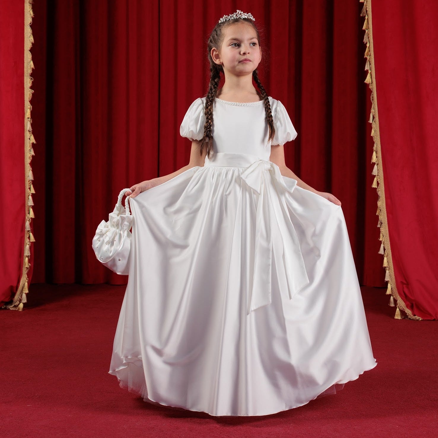 Young girl in a white dress standing in front of red curtains