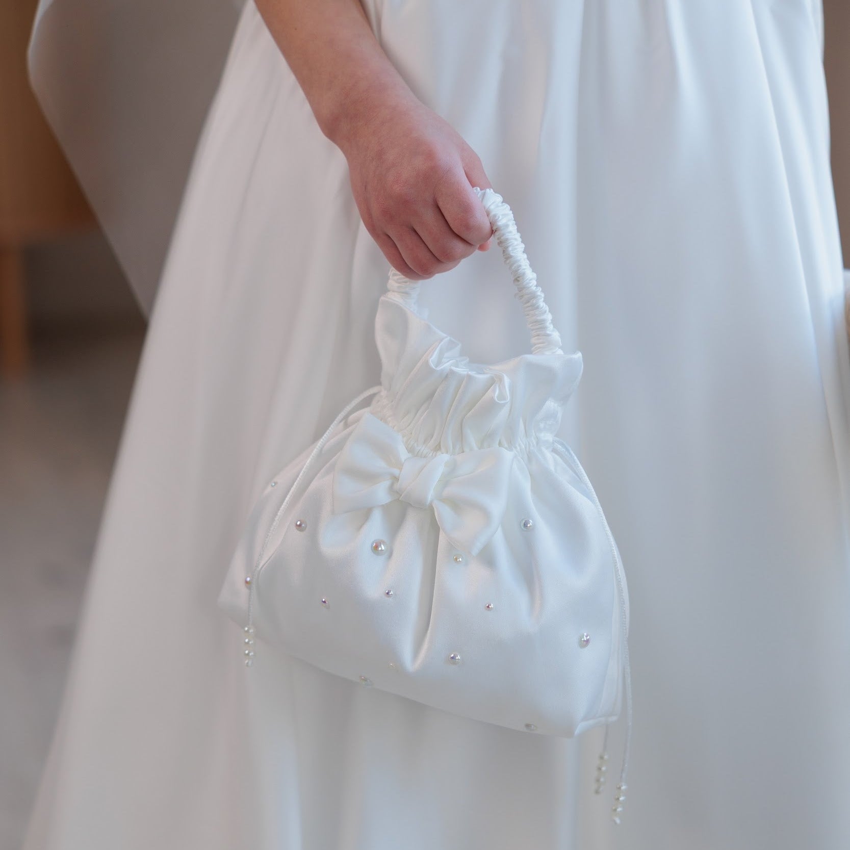 White lace handbag held by a person wearing a white dress.