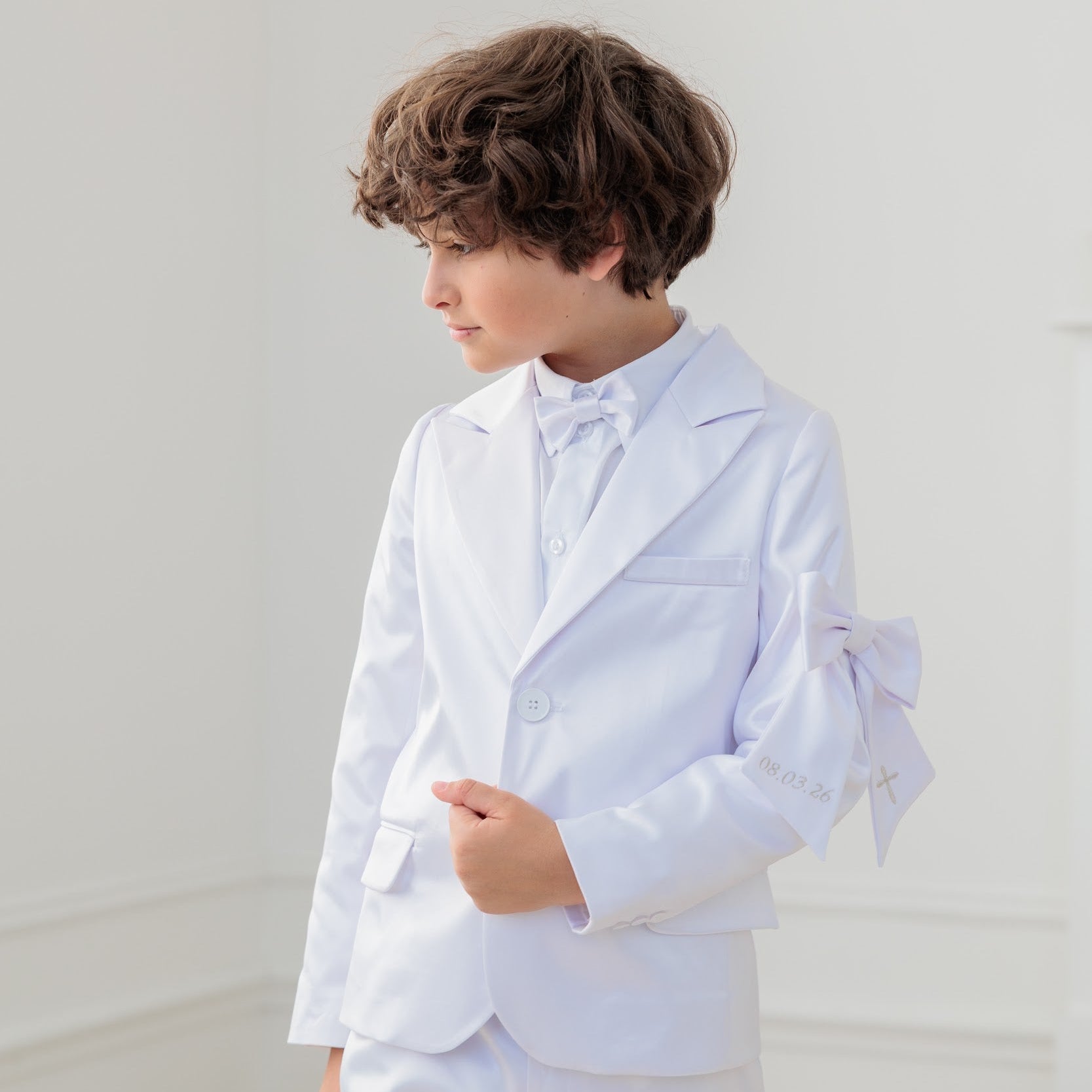 Young boy in a white communion suit with a bow tie against a plain background