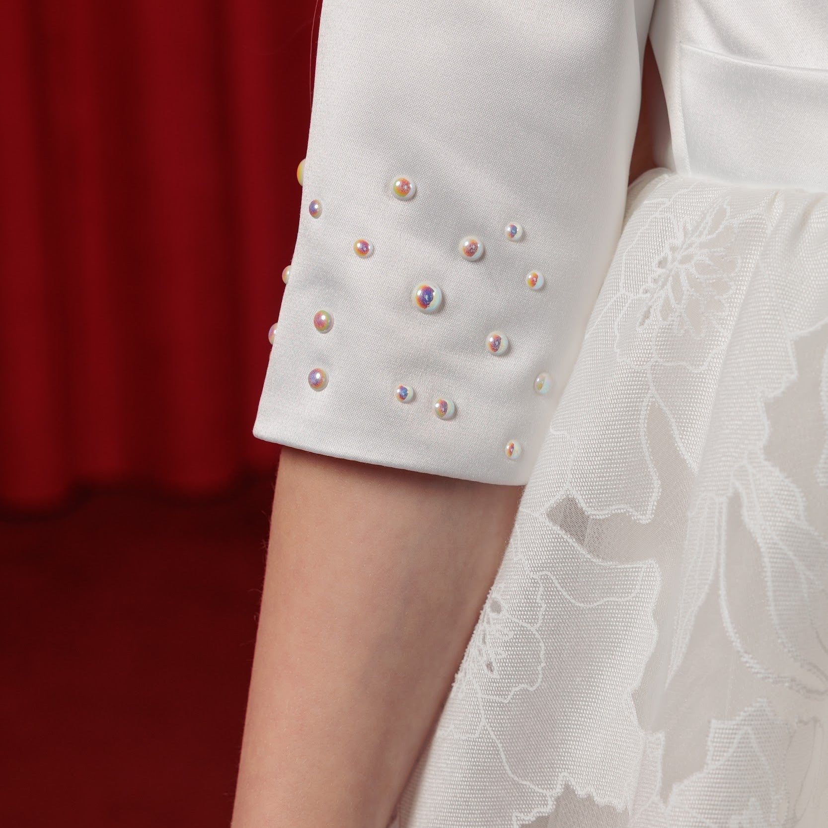 Close-up of a white dress with embellished sleeves against a red background