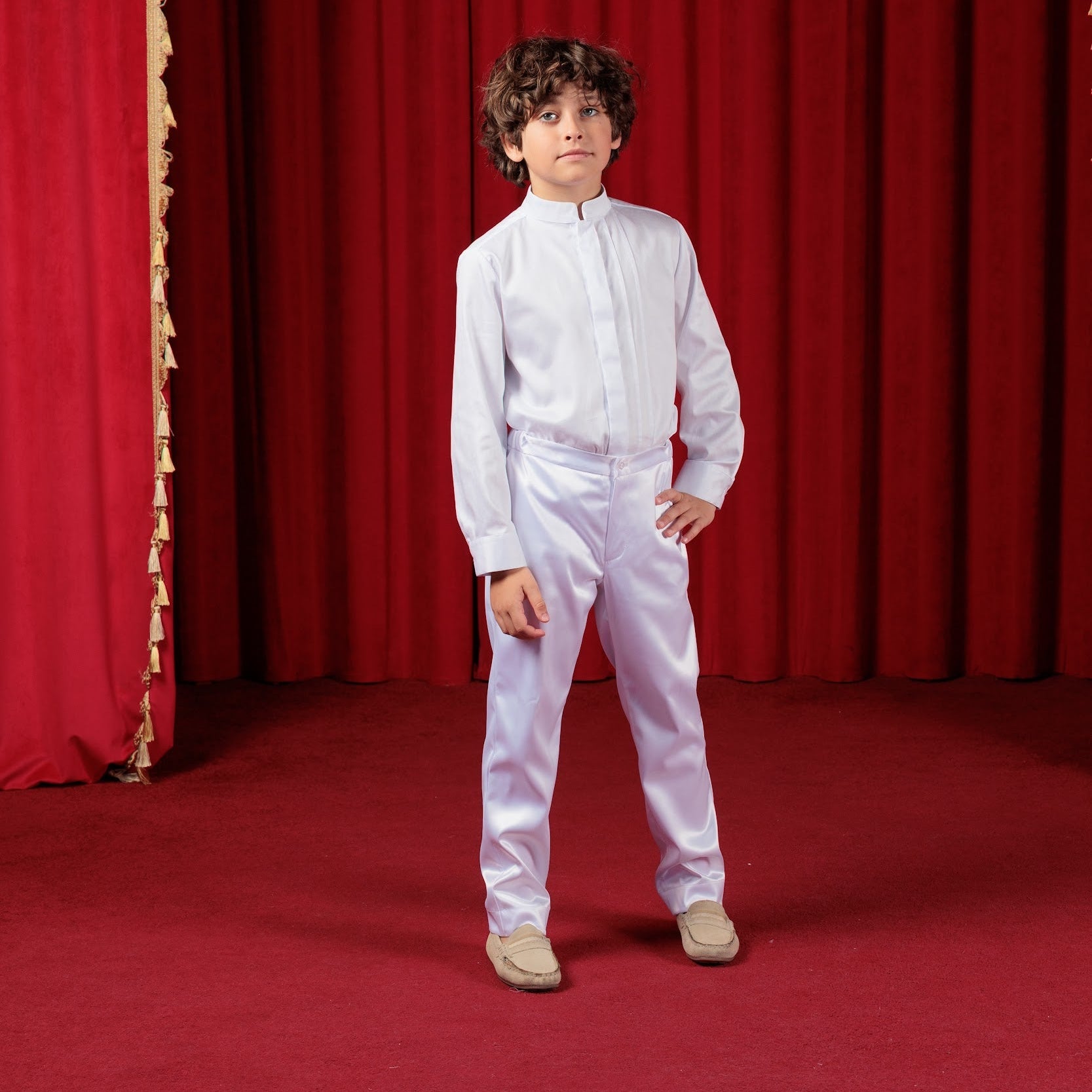 Child in a white outfit standing in front of a red curtain