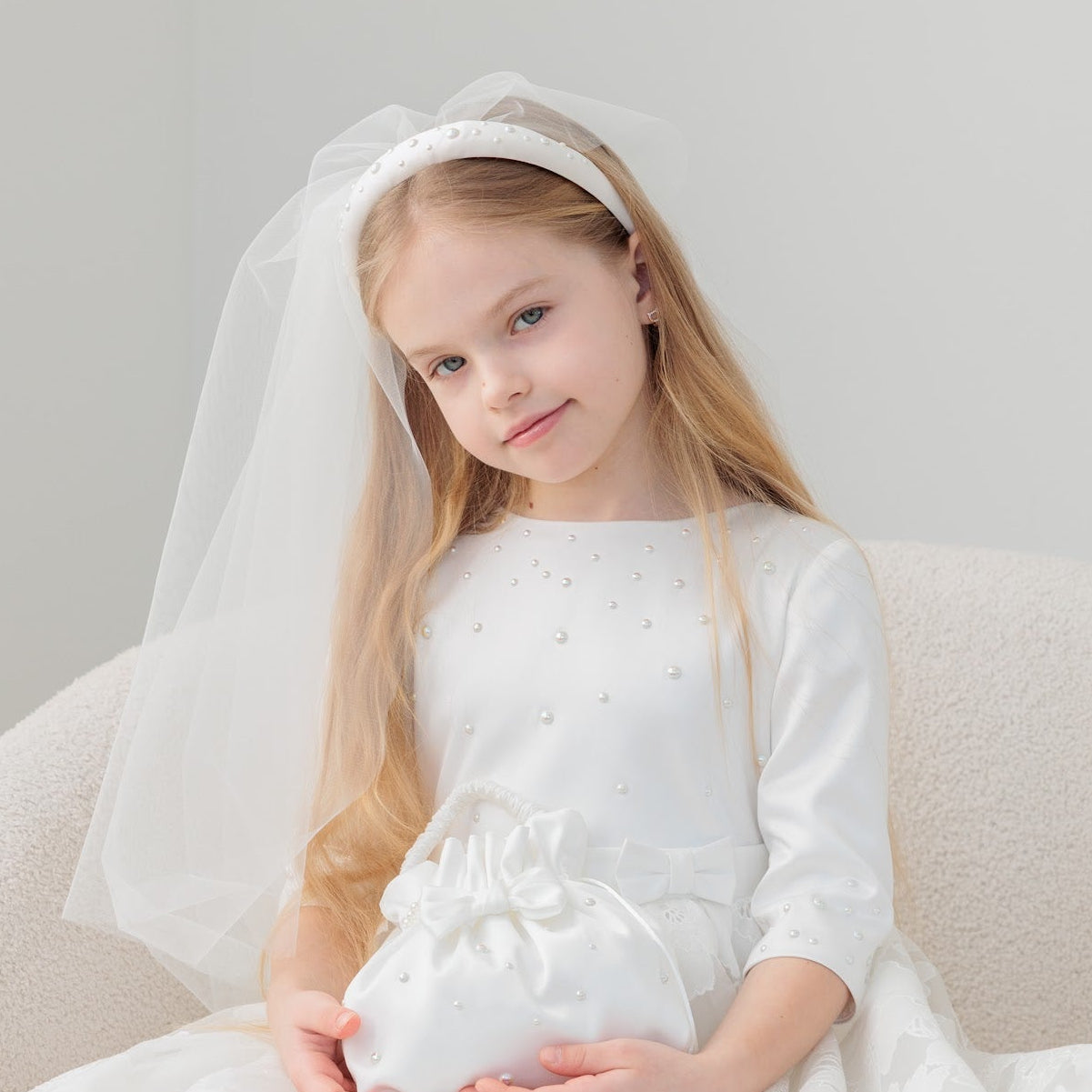 Young girl in a white dress with a veil sitting on a white chair.