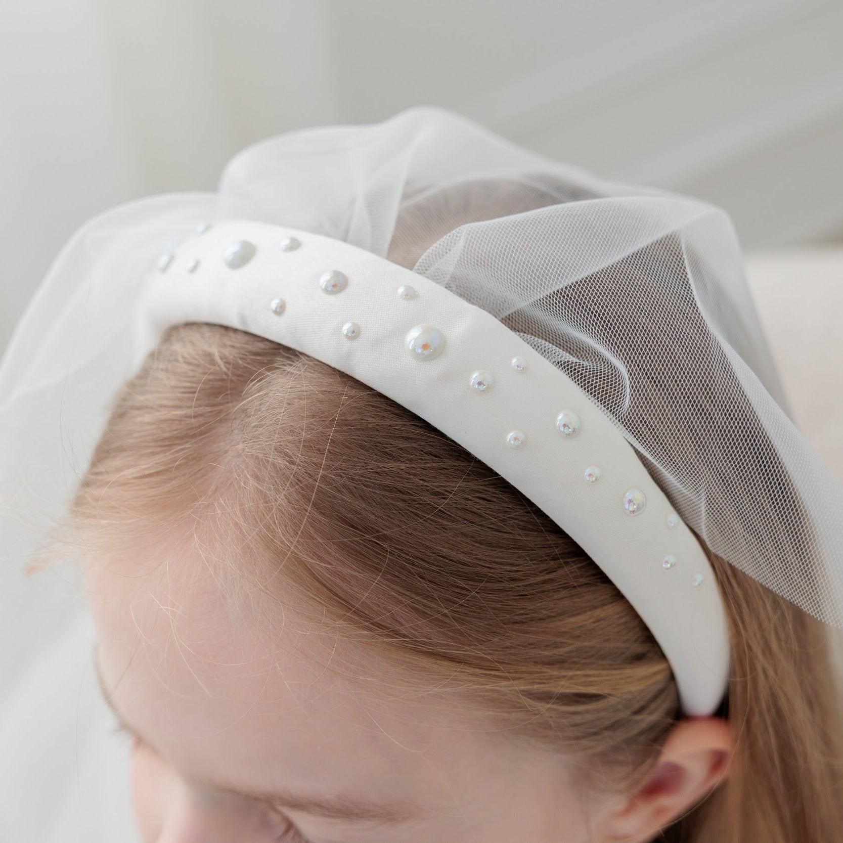 White headband with pearls and tulle on a neutral background