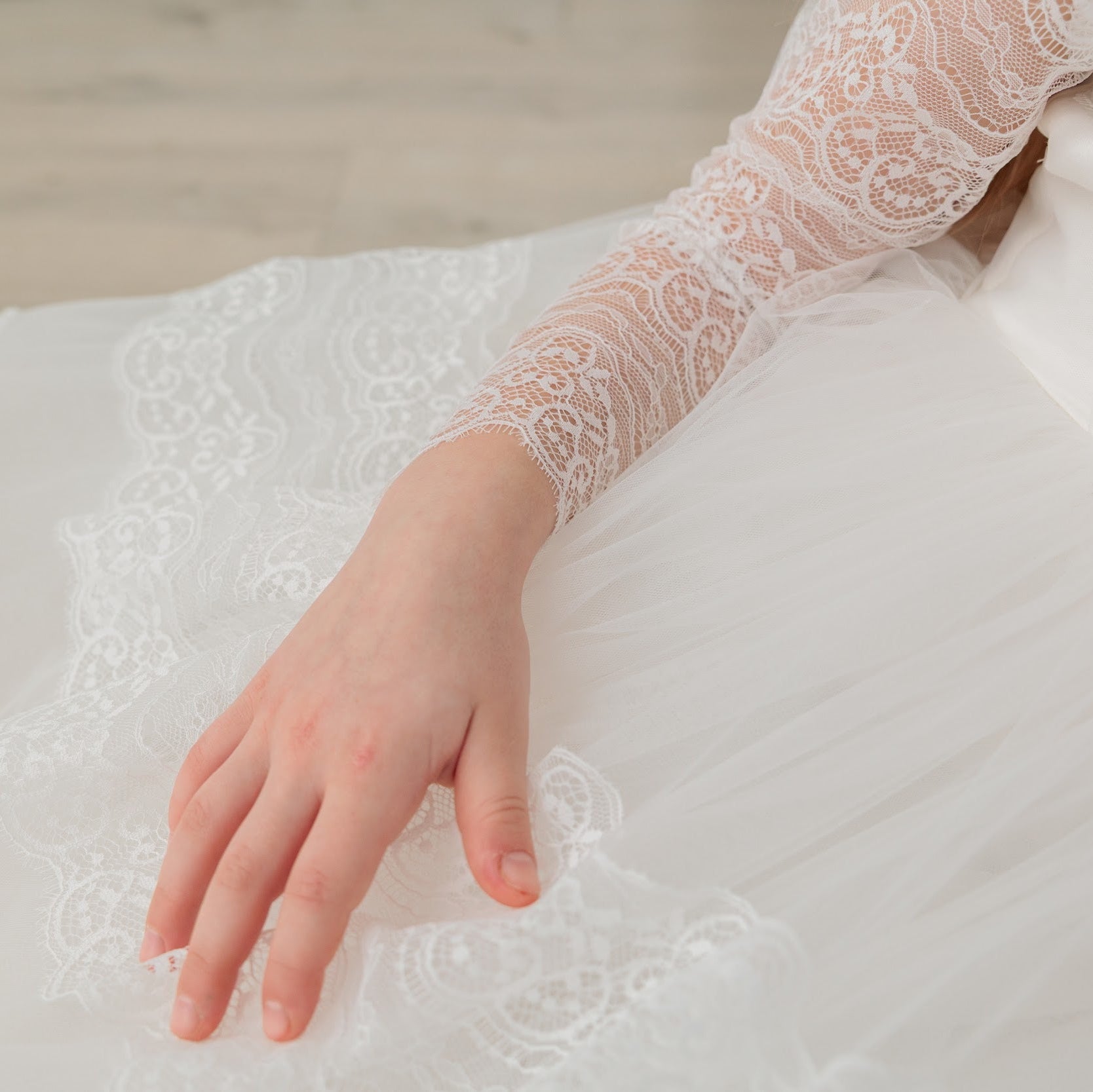 Close-up of a hand wearing a lace glove on a white dress with floral details.