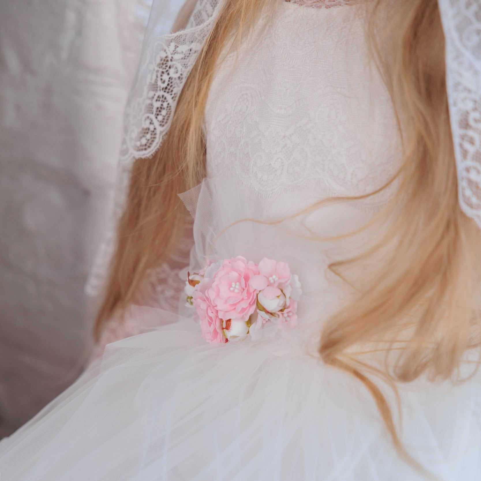Close-up of a person wearing a white lace dress with a pink flower accessory.