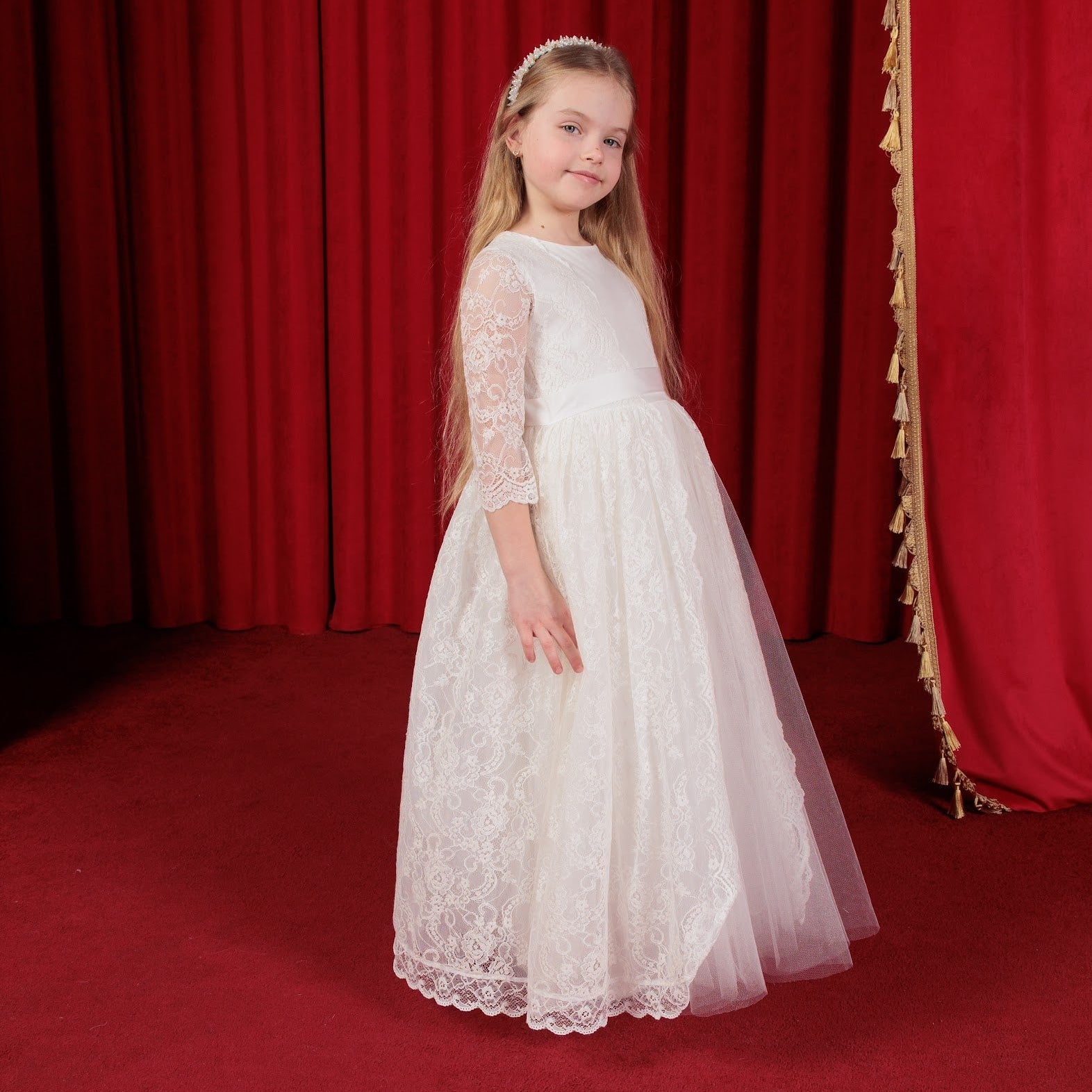 Young girl in a white lace dress standing in front of red curtains