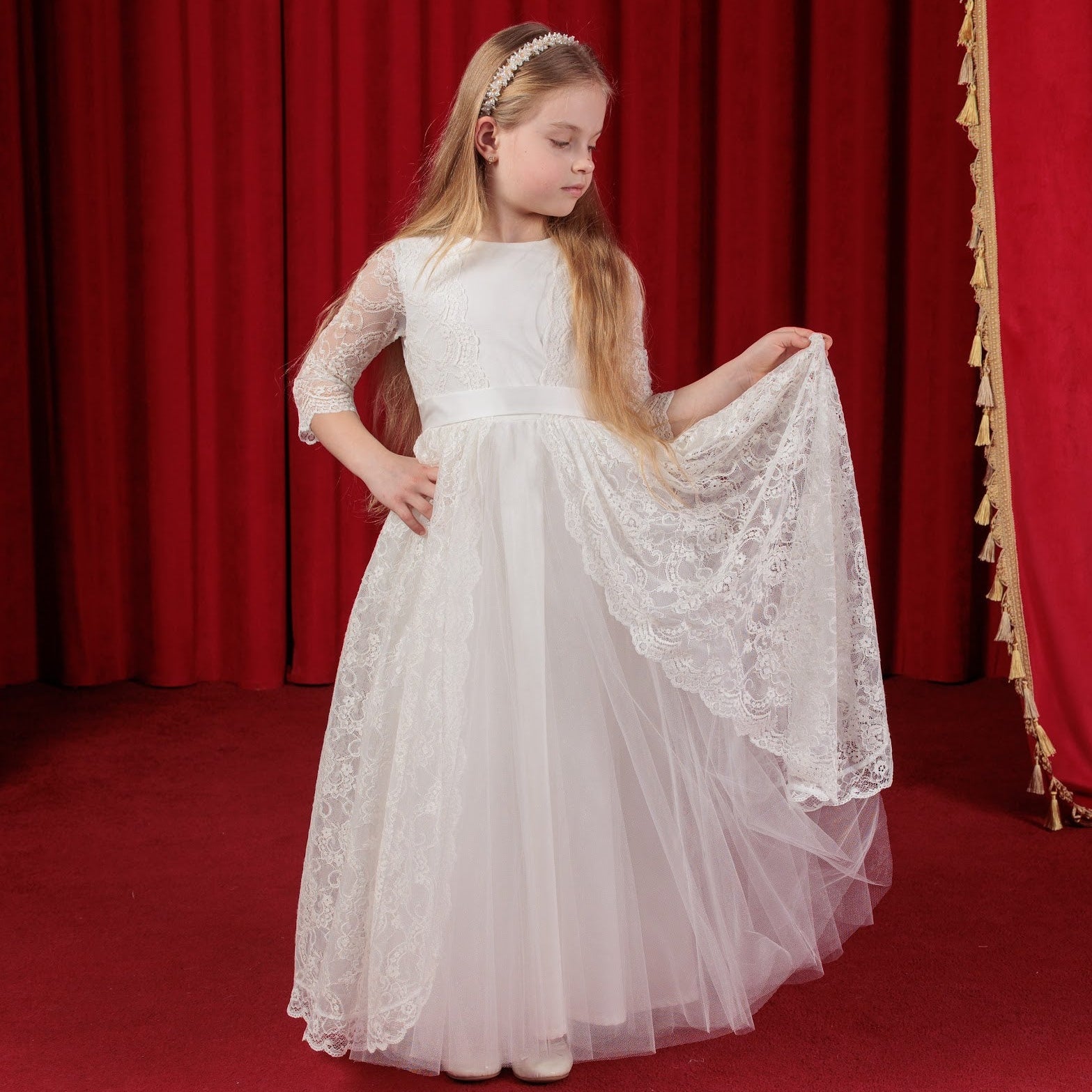 Young girl in a white dress standing in front of red curtains