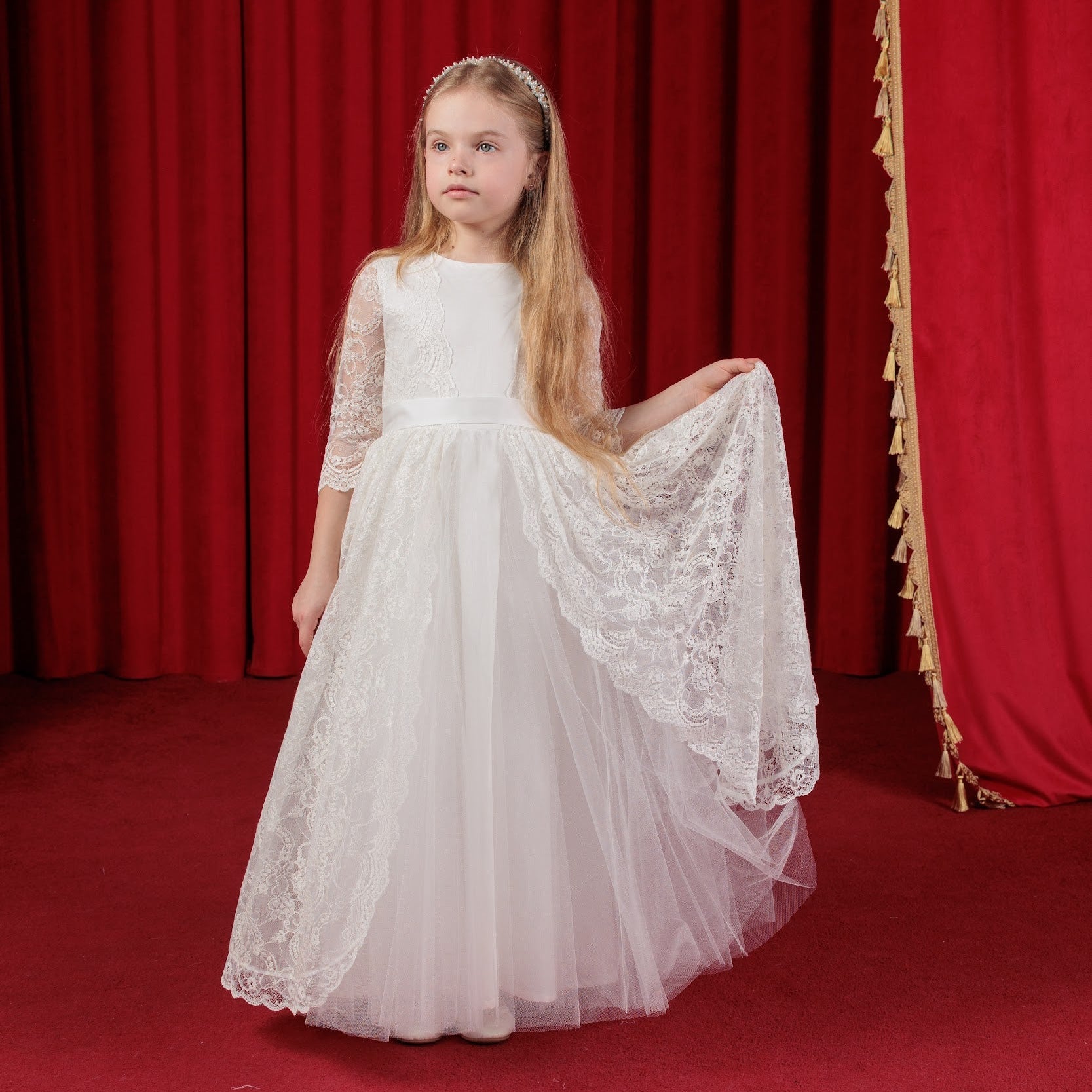 Young girl in a white lace dress standing in front of red curtains
