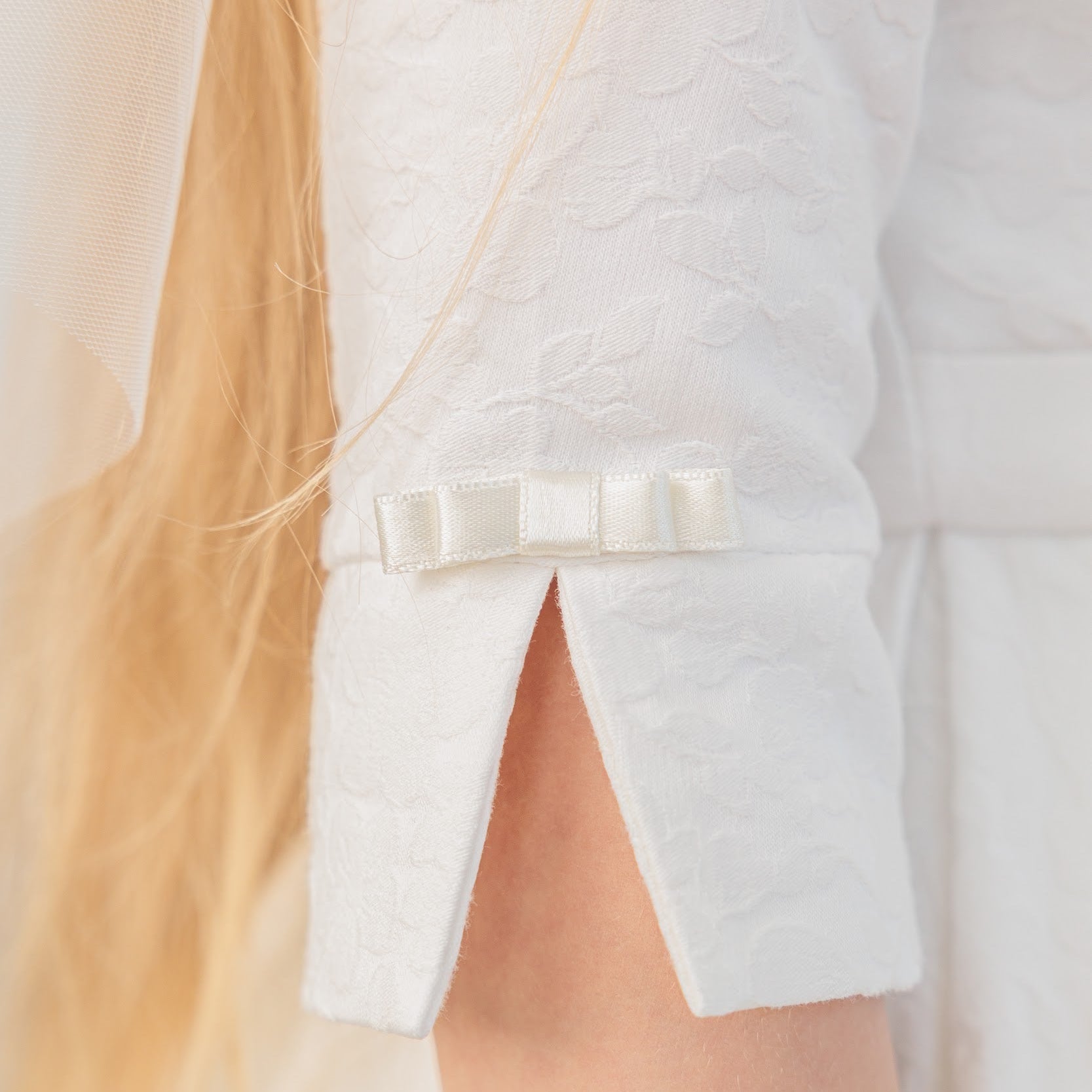 Close-up of a white blazer with a bow detail on a blurred background