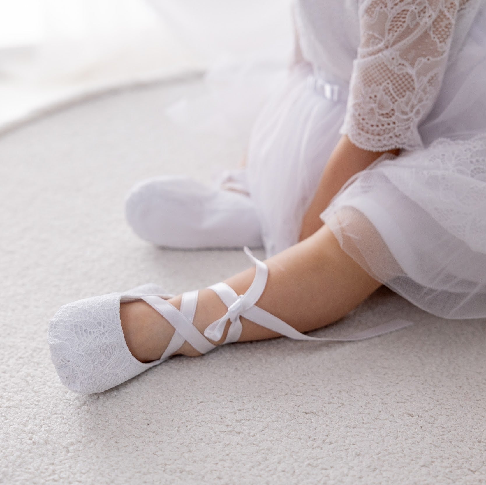 Person wearing white ballet shoes and a white dress on a light background