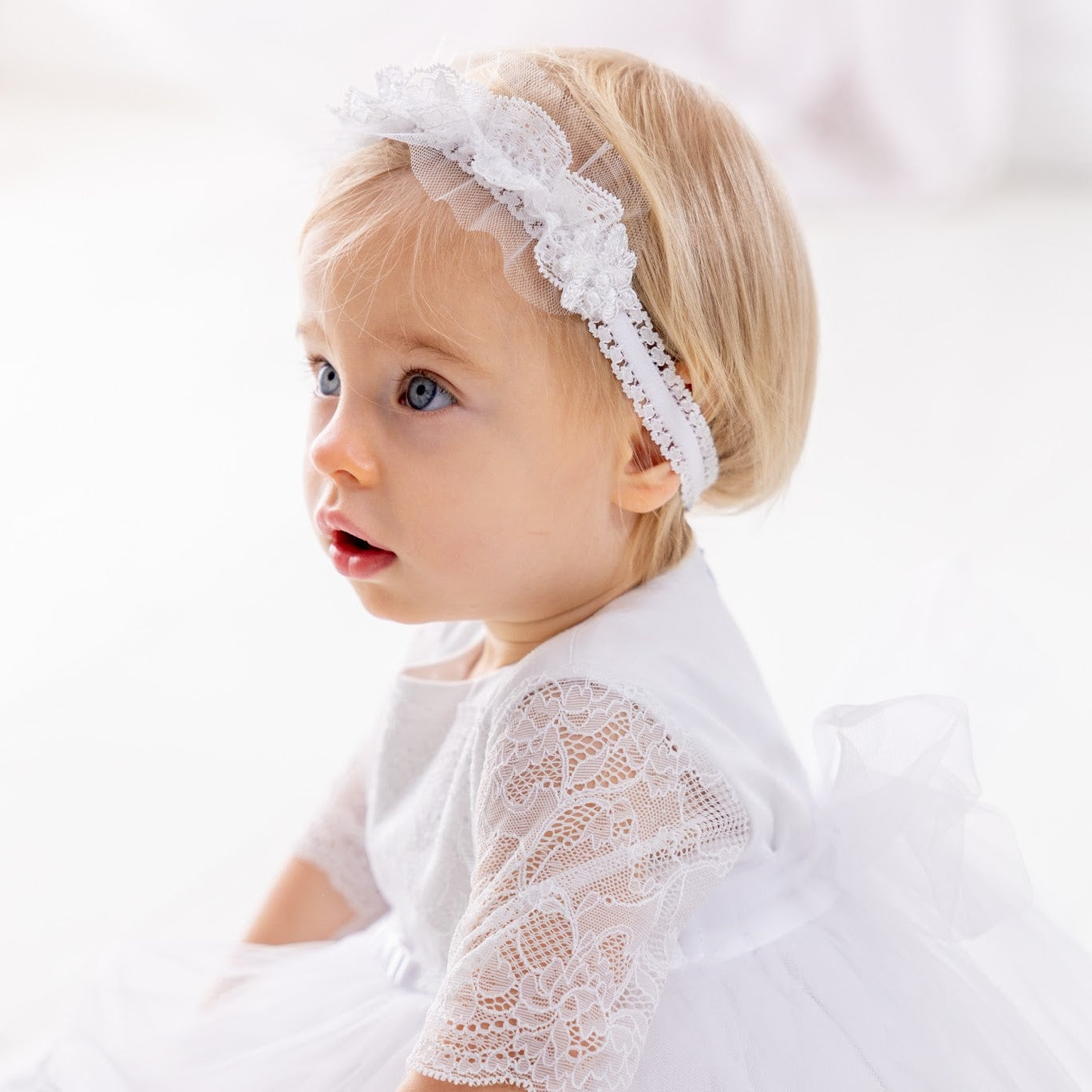 Young child in a white lace dress with a matching headband against a light background