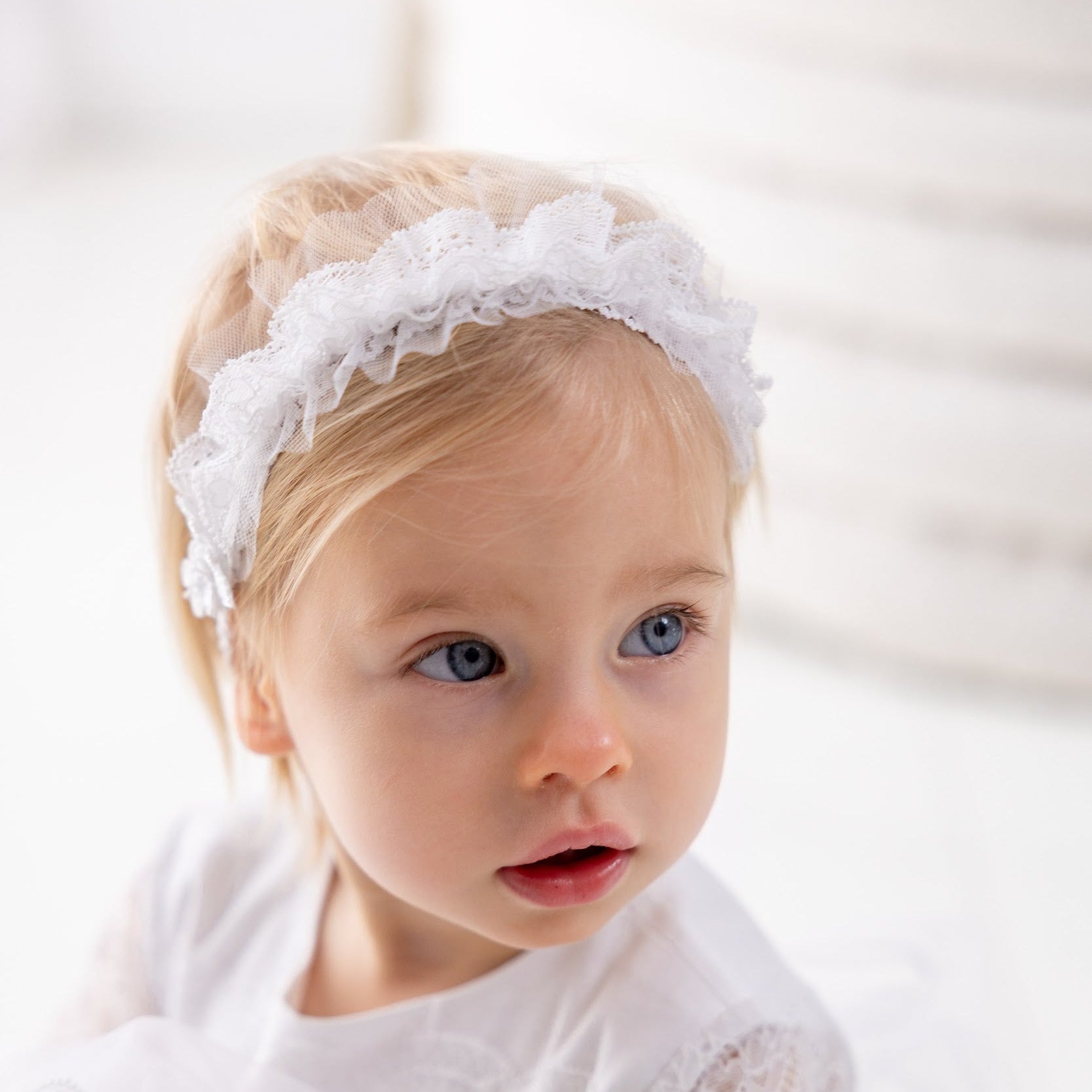Young girl wearing a white lace headband and dress against a light background