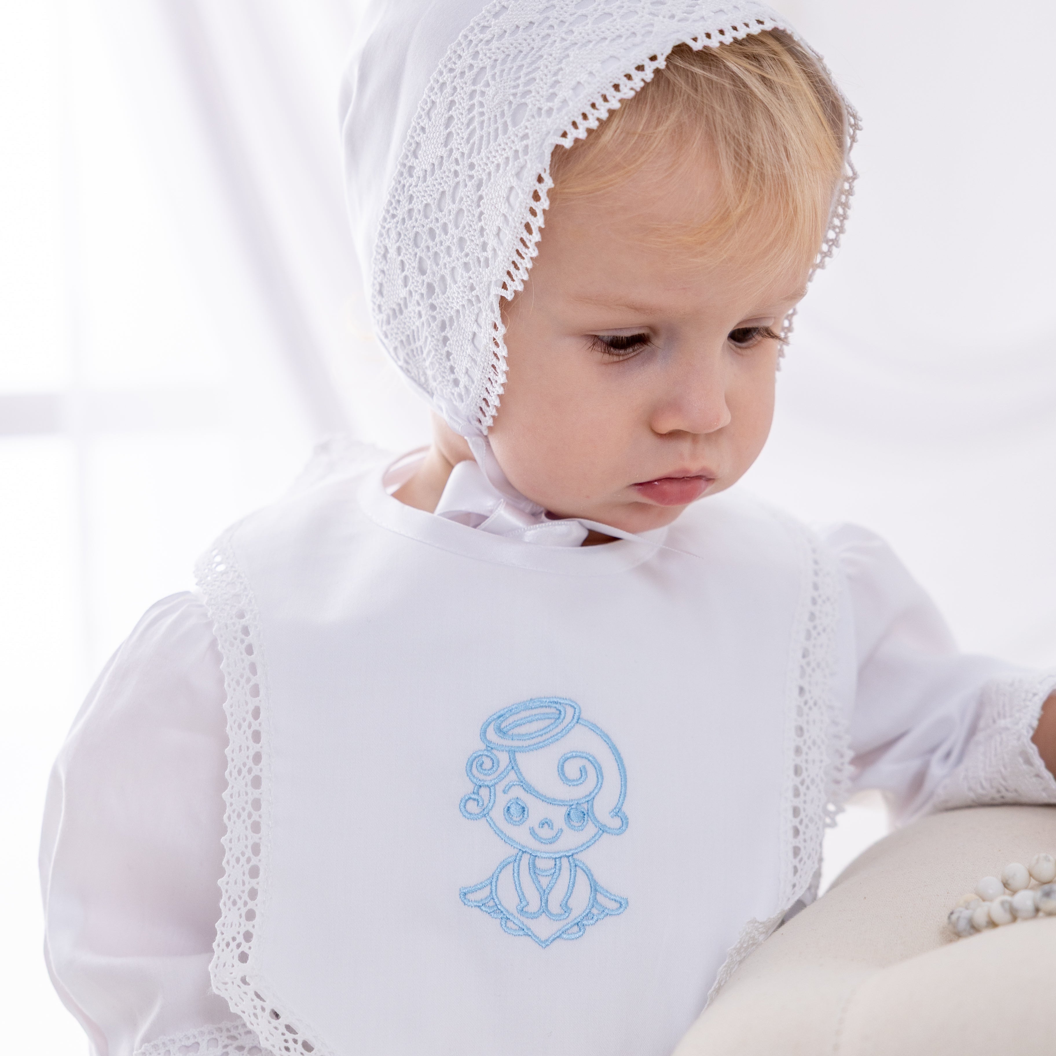 Baby wearing a white embroidered bonnet and bib on a white background