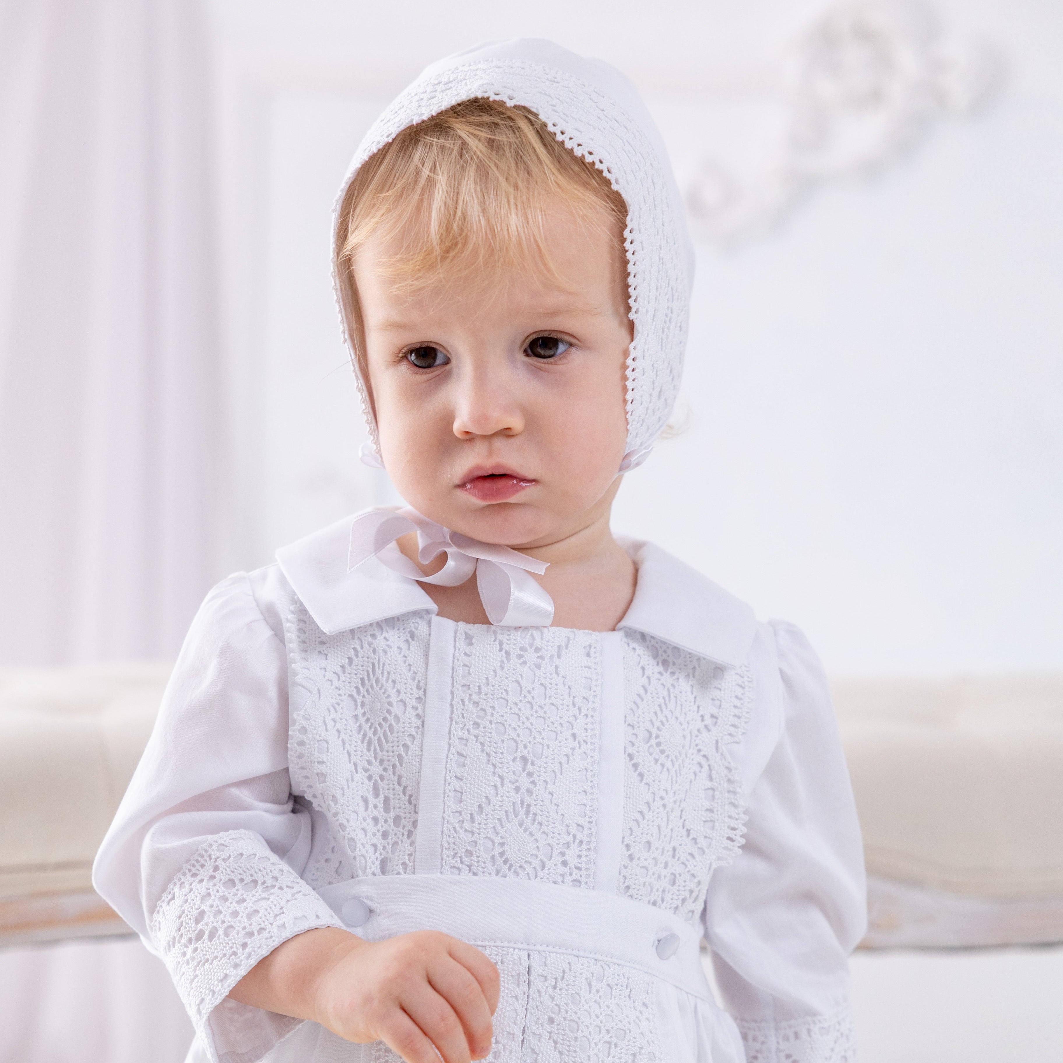 Child wearing a white dress with a bonnet on a light background
