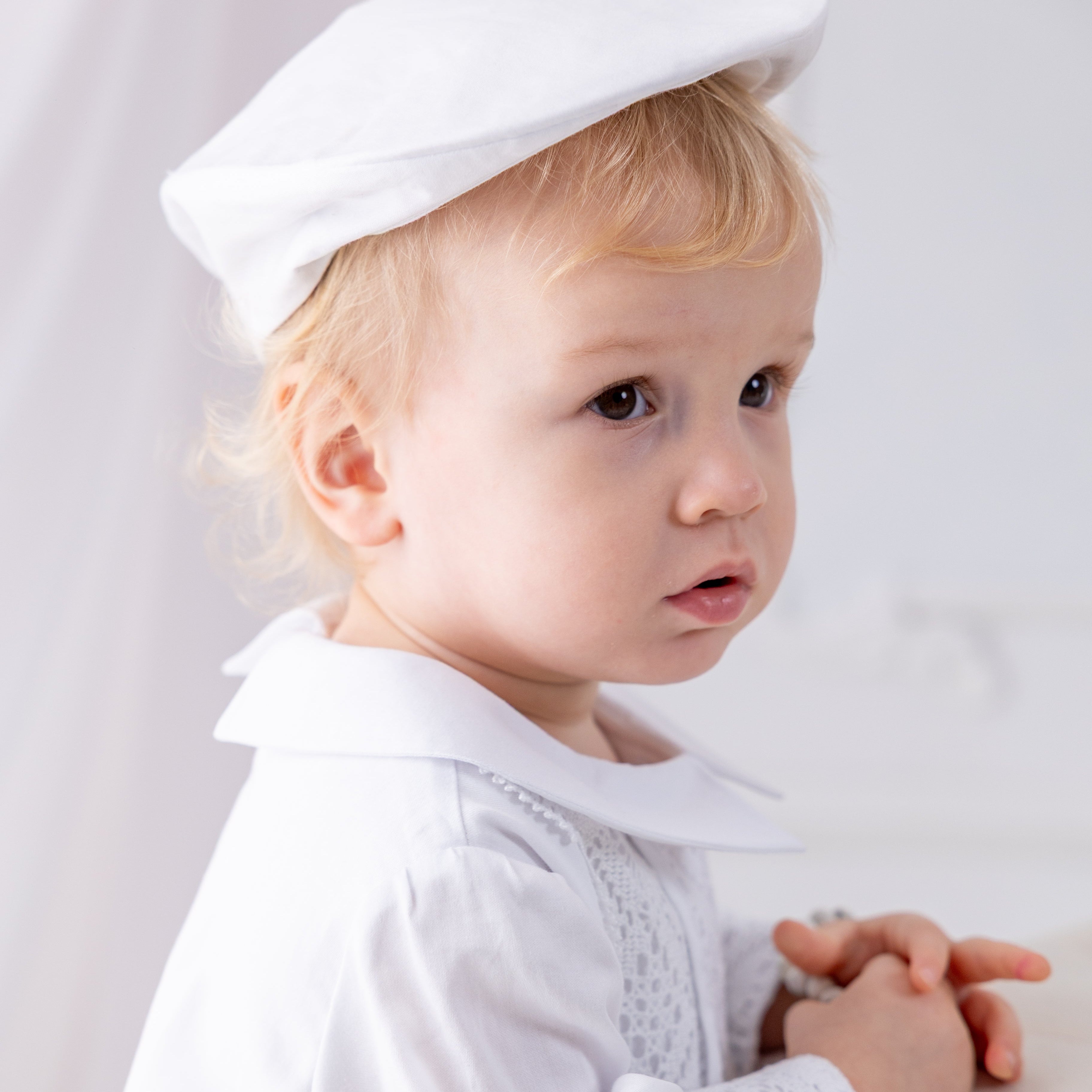Child wearing a white outfit with a hat against a light background