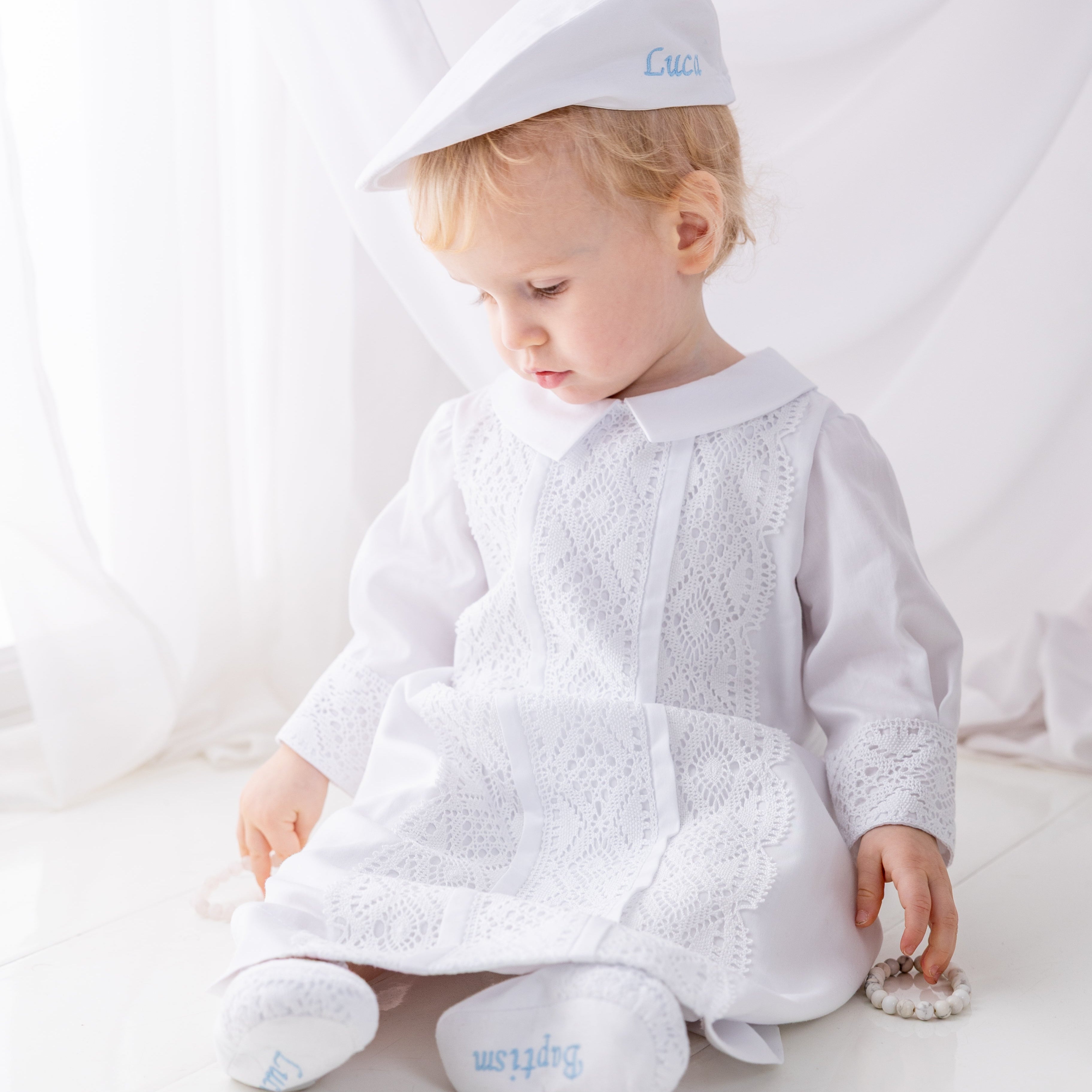 Baby in white outfit with embroidered name on a white background