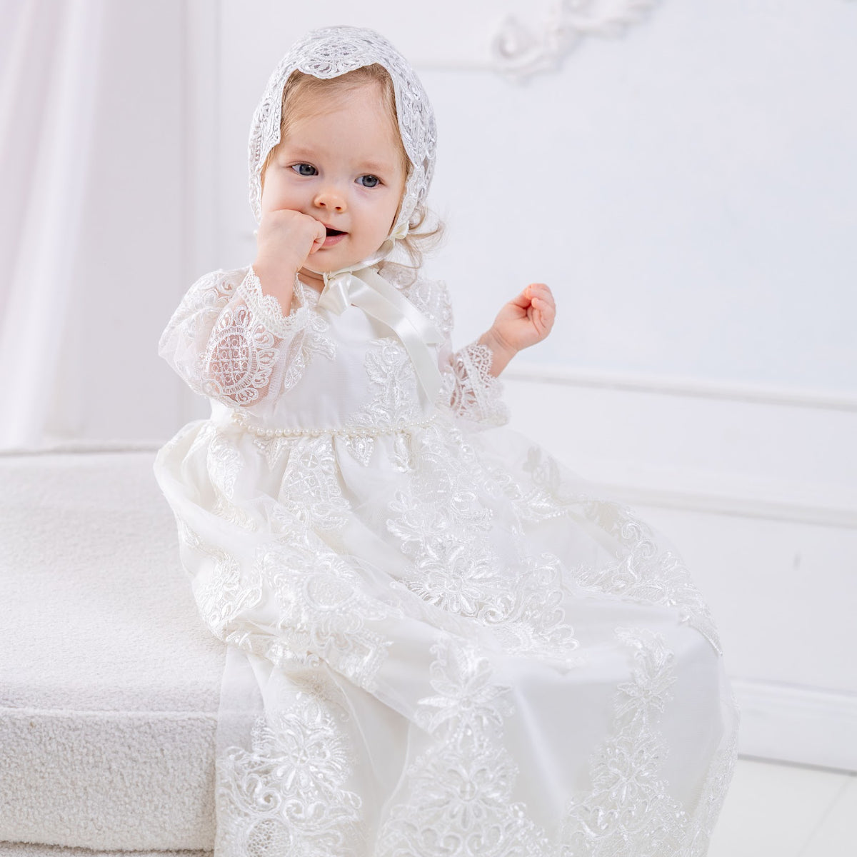 Baby in a Long Lace Christening Gown for Girls sitting on a white surface