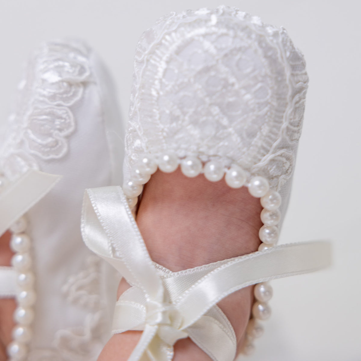 Baby's feet in Christening Booties with pearls and ribbons on a light background