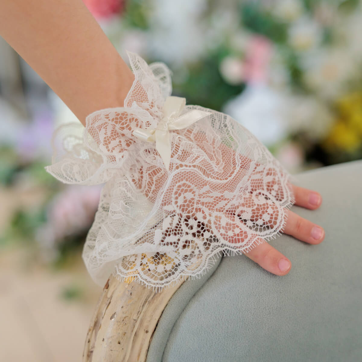Lace wrist cuff worn on a wrist with a blurred floral background