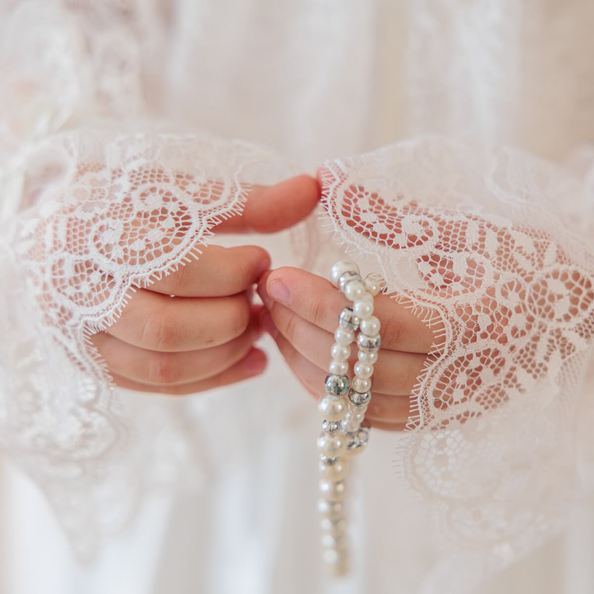 Hand wearing a pearl bracelet with lace cuffs on a white background