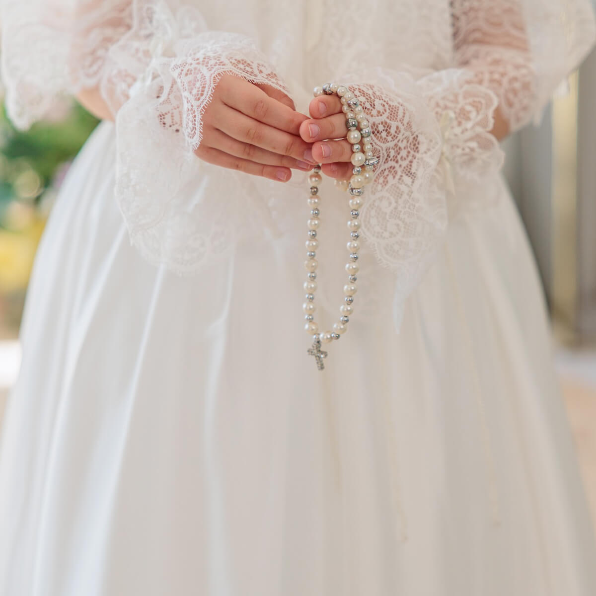Person wearing a white lace dress holding a rosary.