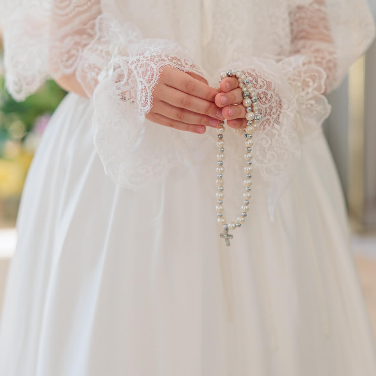 Person wearing a white lace dress holding a rosary.