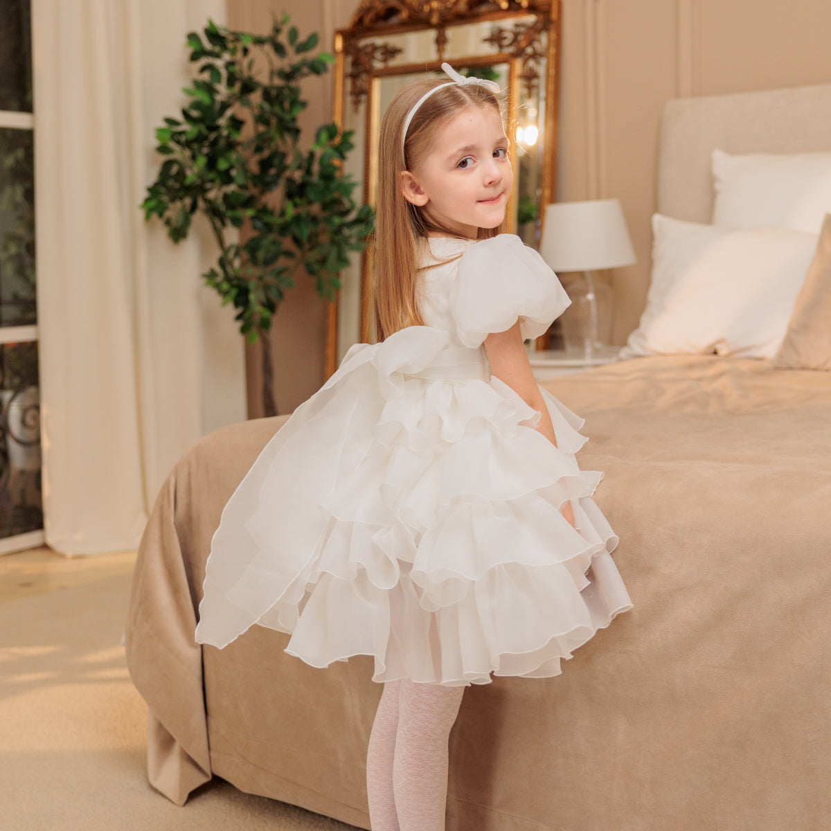 Young girl in a white dress standing in a bedroom