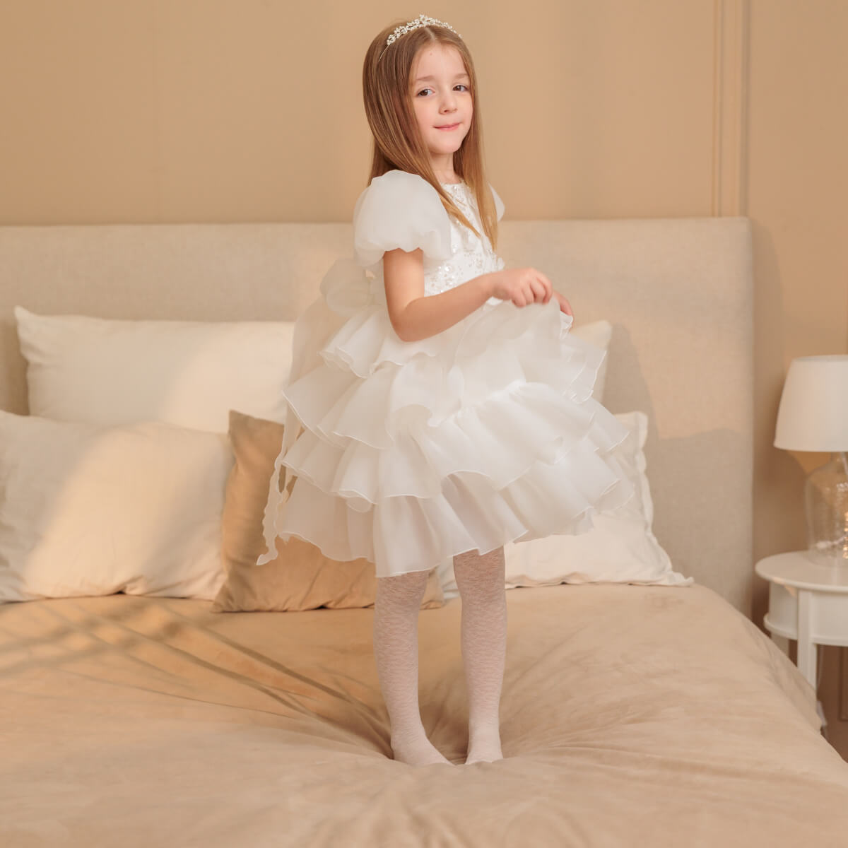 Young girl in a white dress standing on a bed in a bedroom setting