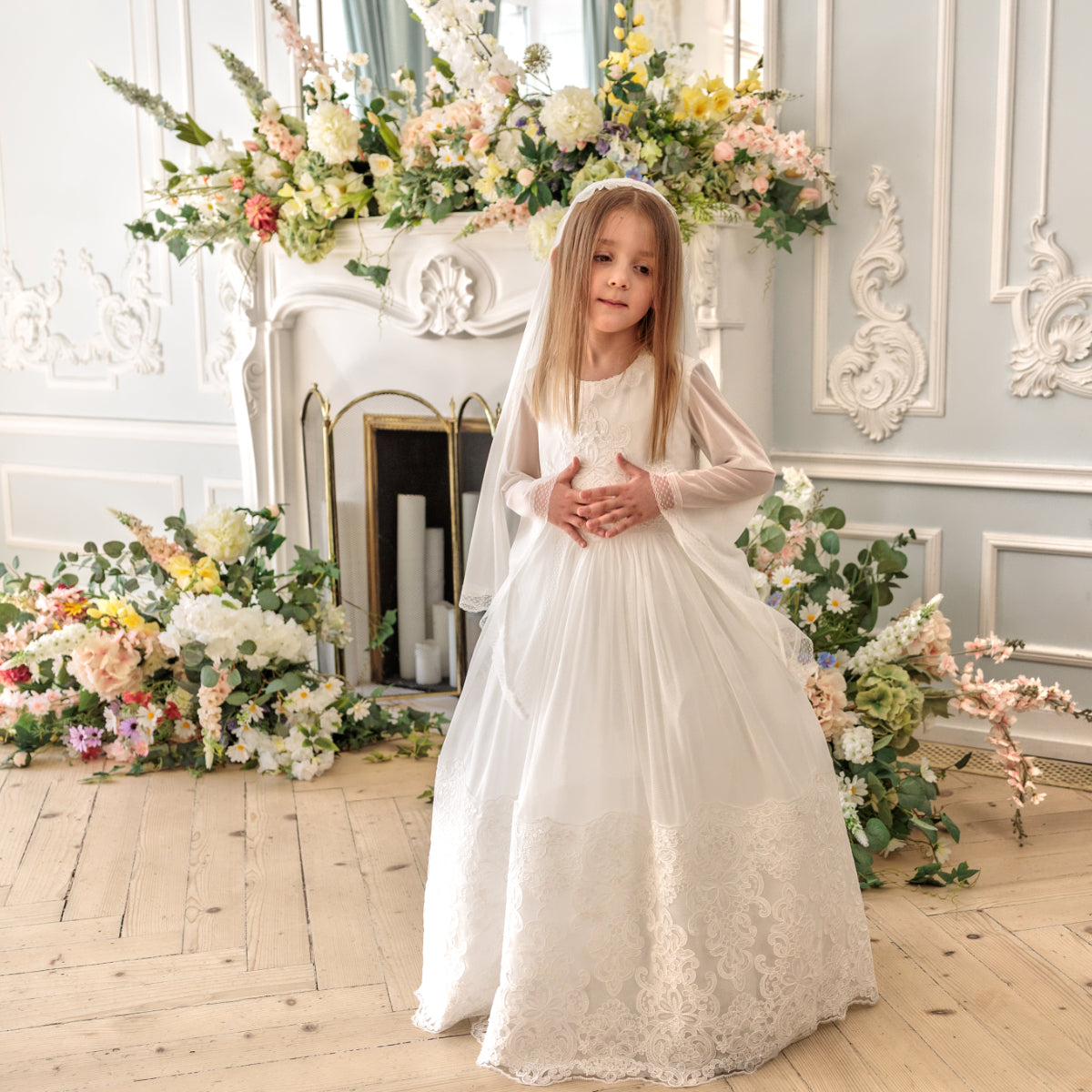 Young girl in Holy Communion Dress standing in a decorated room with floral arrangements.