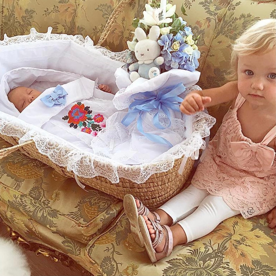 Baby in a crib with Newborn Sleep Sack for Summer next to a toddler in a pink dress on a patterned couch.
