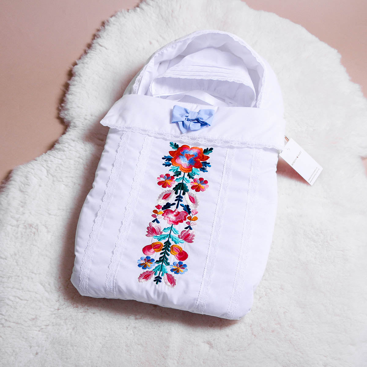 Newborn Sleep Sack for Summer with floral embroidery and a blue bow on a fluffy white surface.