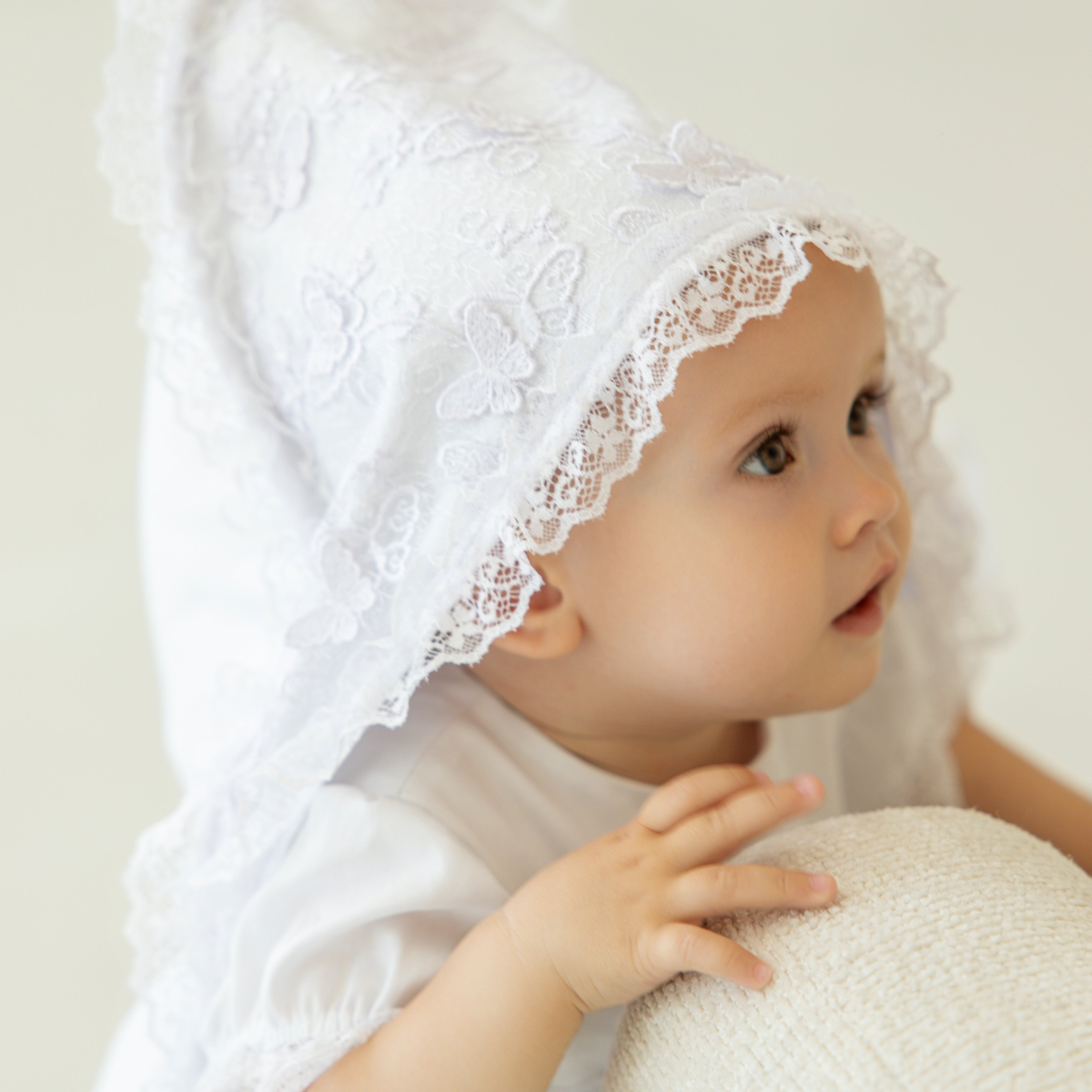 Baby  in lace christening blanket against a plain background