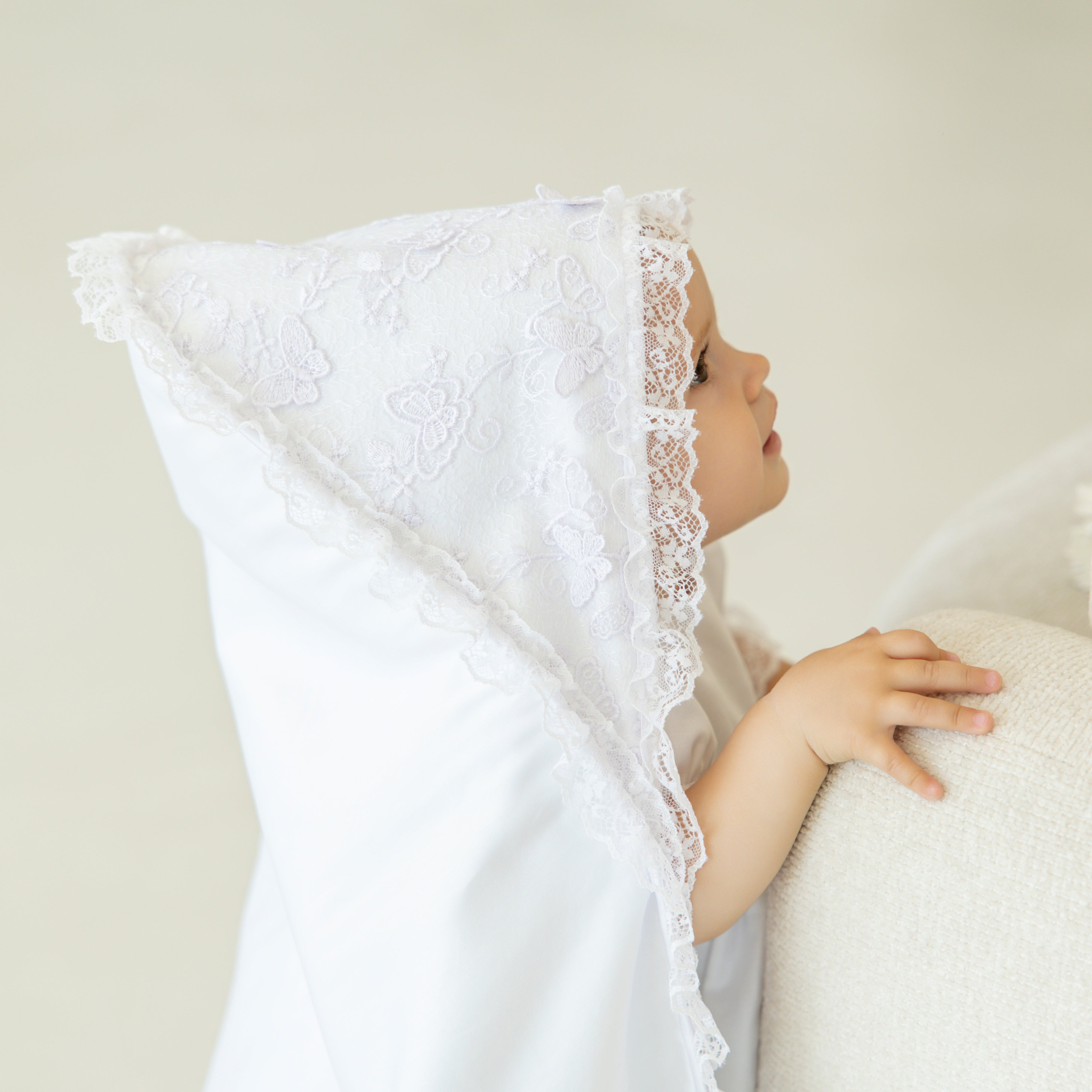 Child in white lace christening blanket against a neutral background