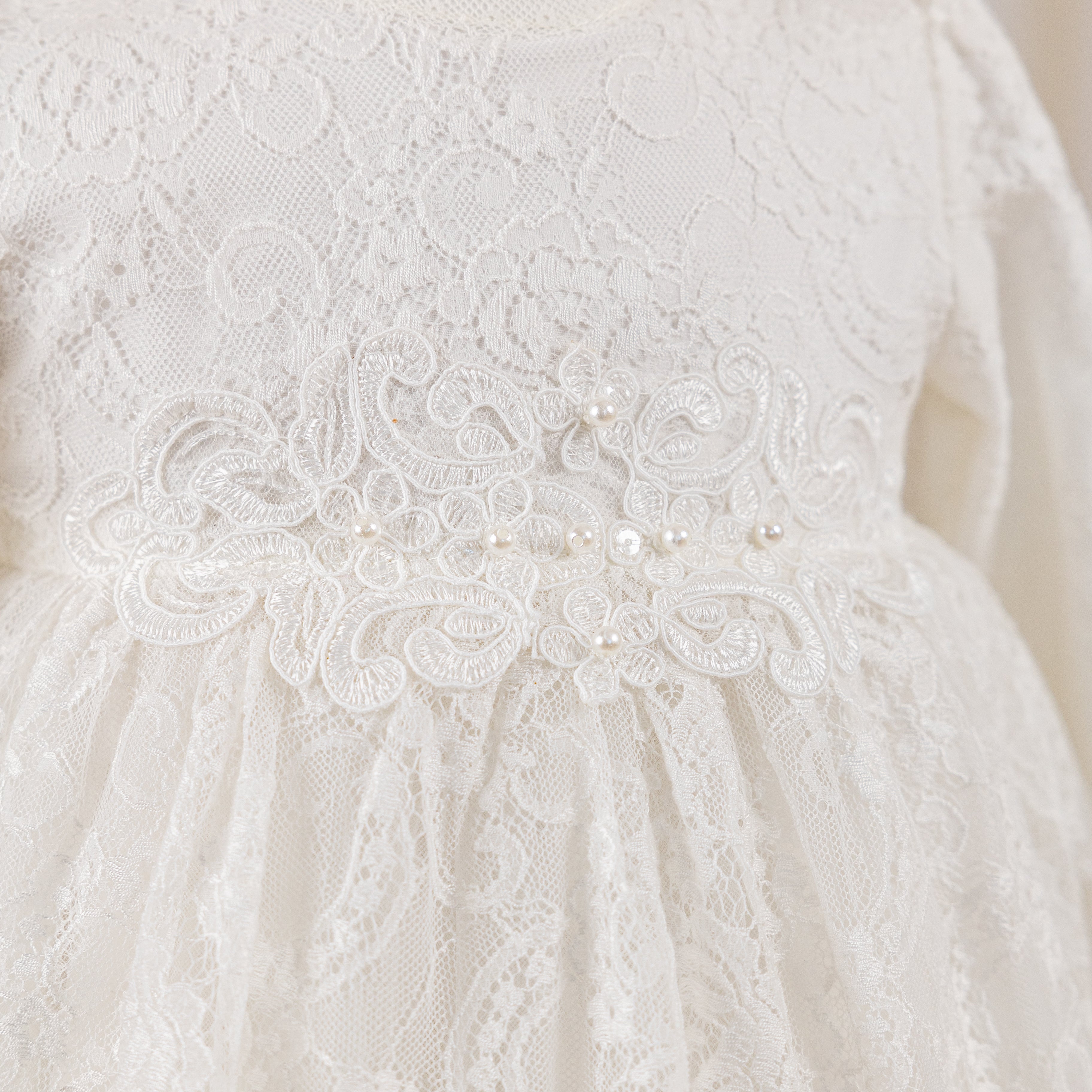 Close-up of a white baptism lace dress with intricate detailing and pearl embellishments.