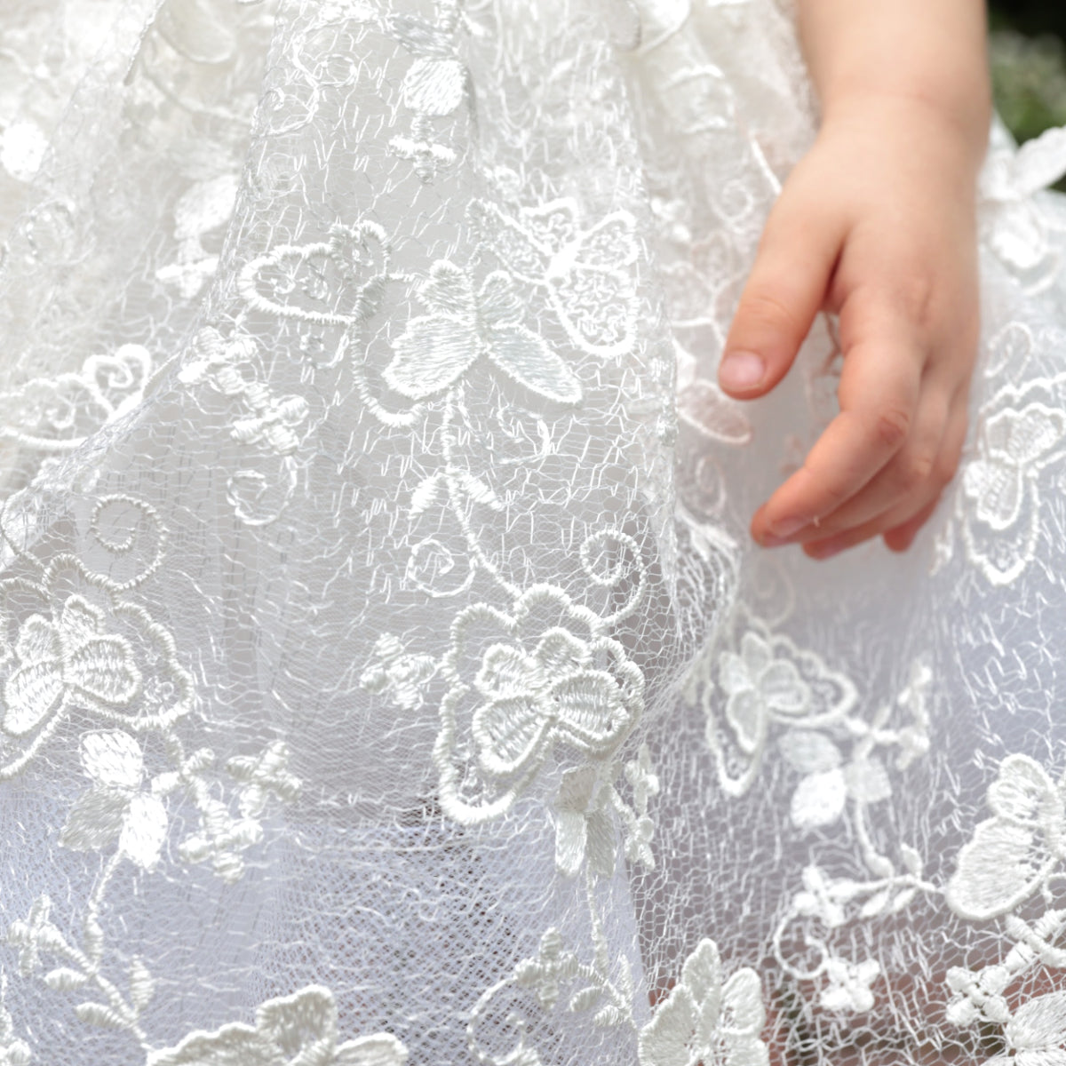Close-up of a hand touching white lace fabric with floral patterns