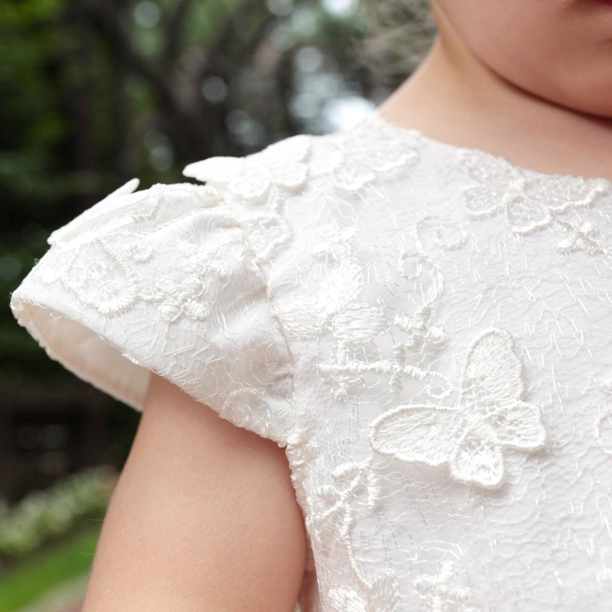 Close-up of a child wearing a white lace dress with butterfly details, blurred green background