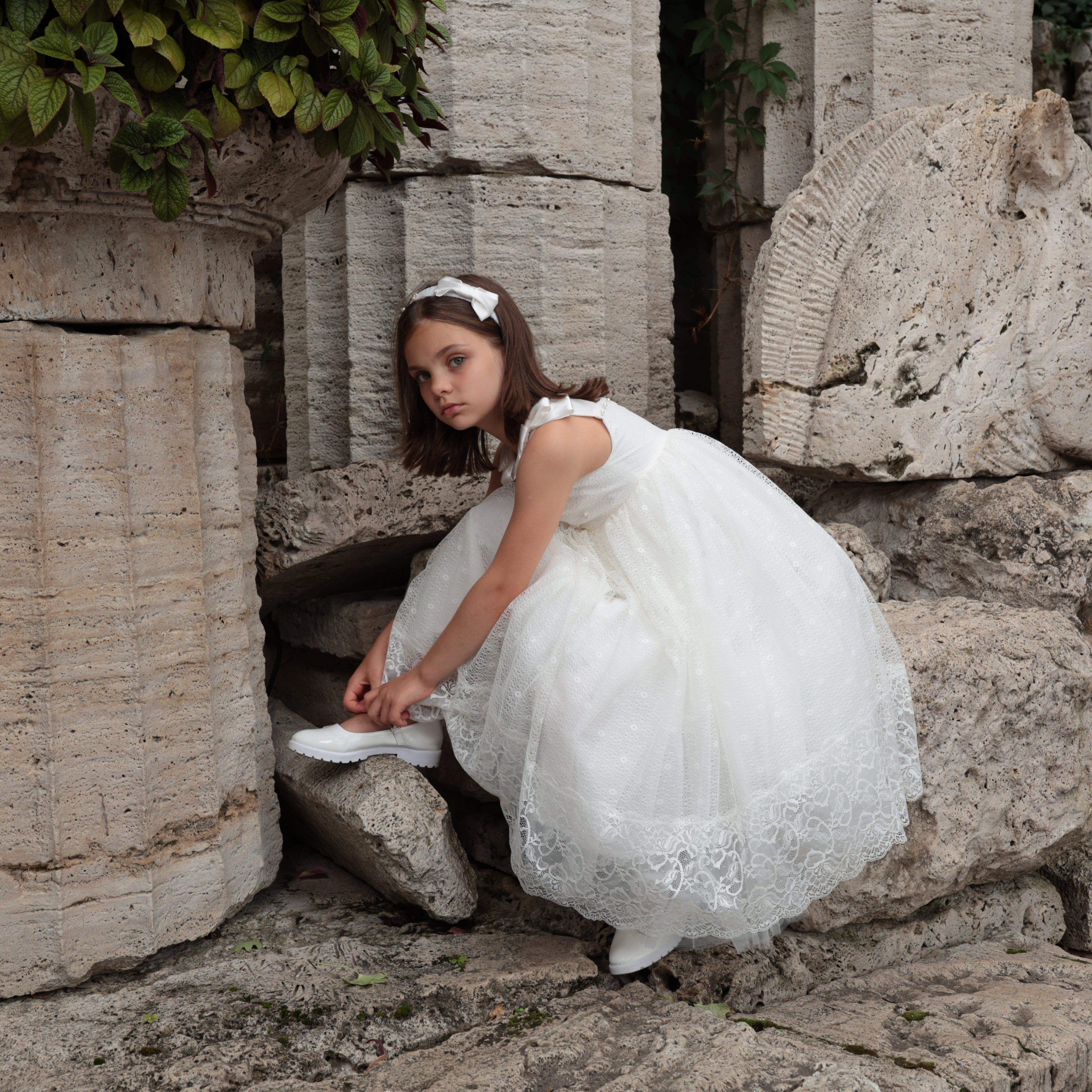 Young girl in a white dress sitting among stone ruins