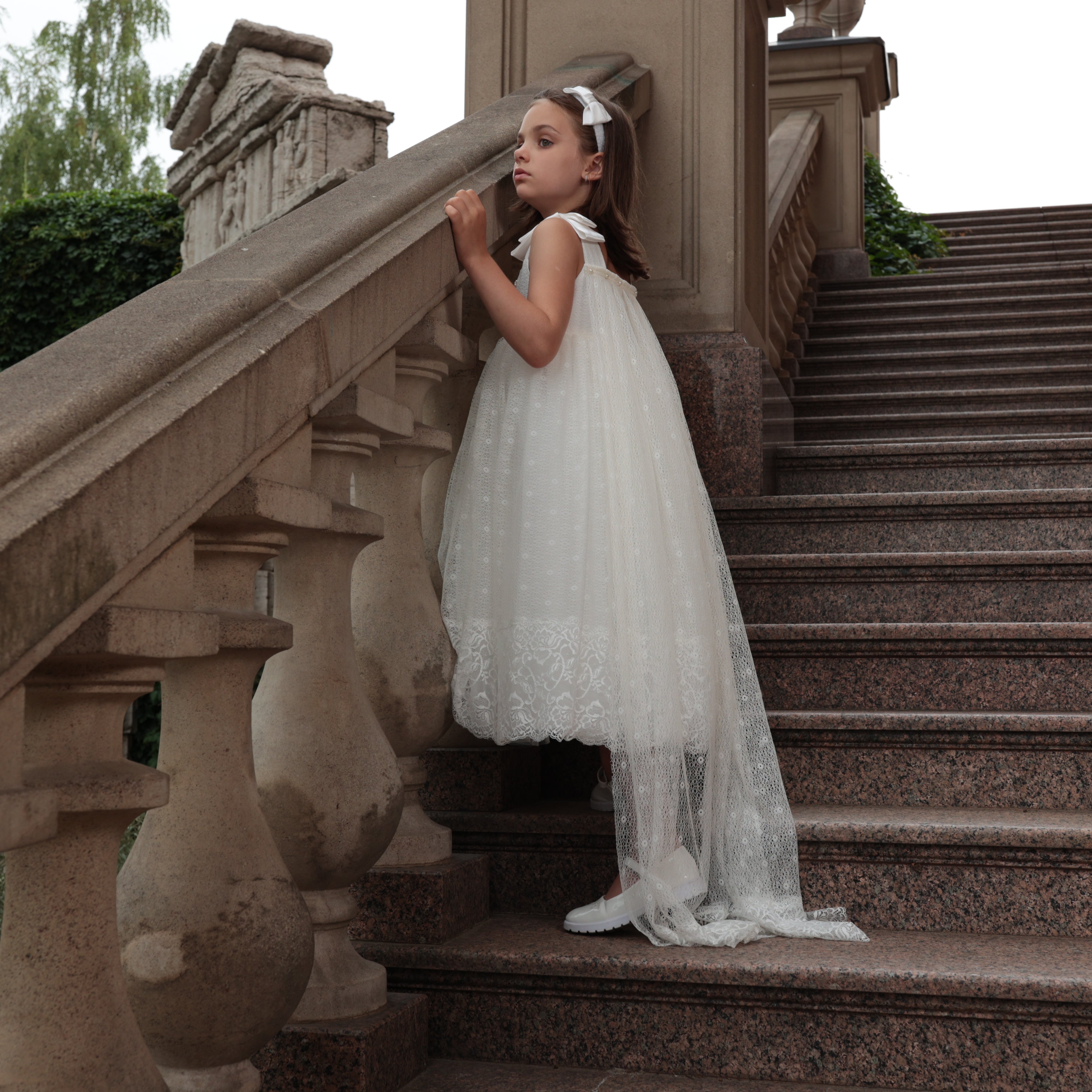 Young girl in ivory dress standing on stone steps outdoors