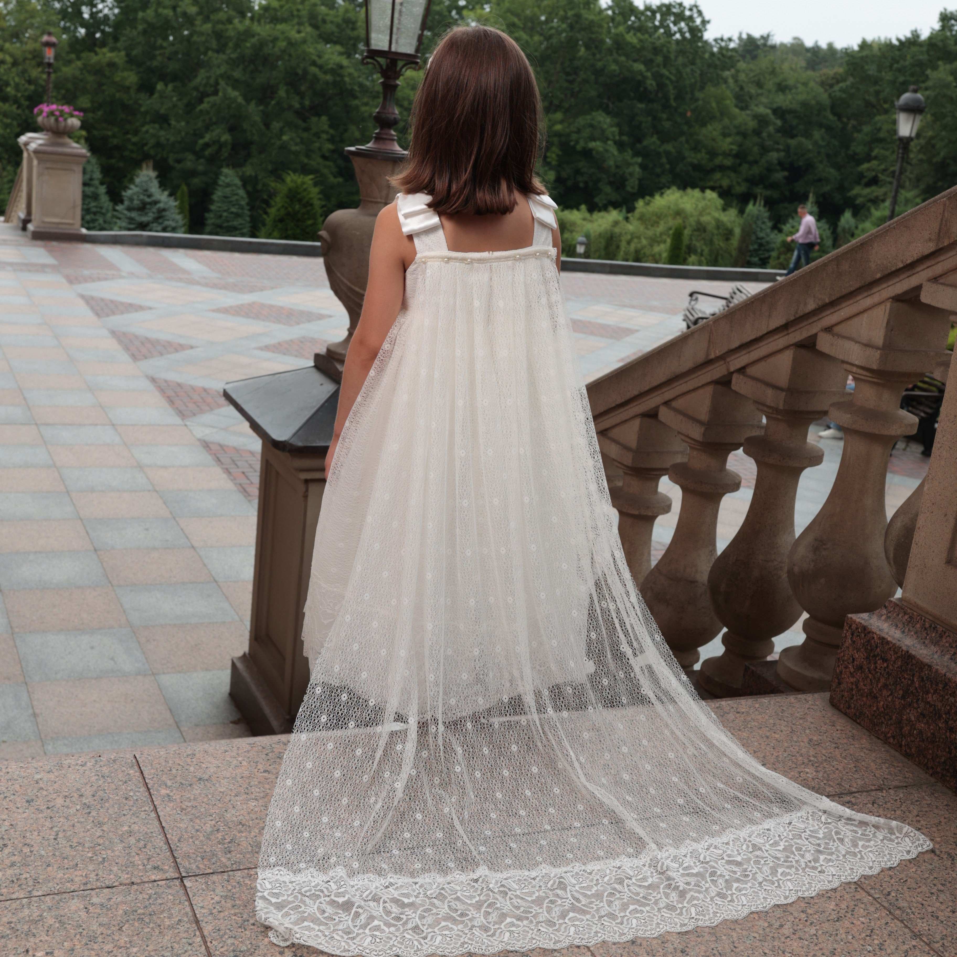 Woman in a white lace dress standing on a stone pathway with trees in the background