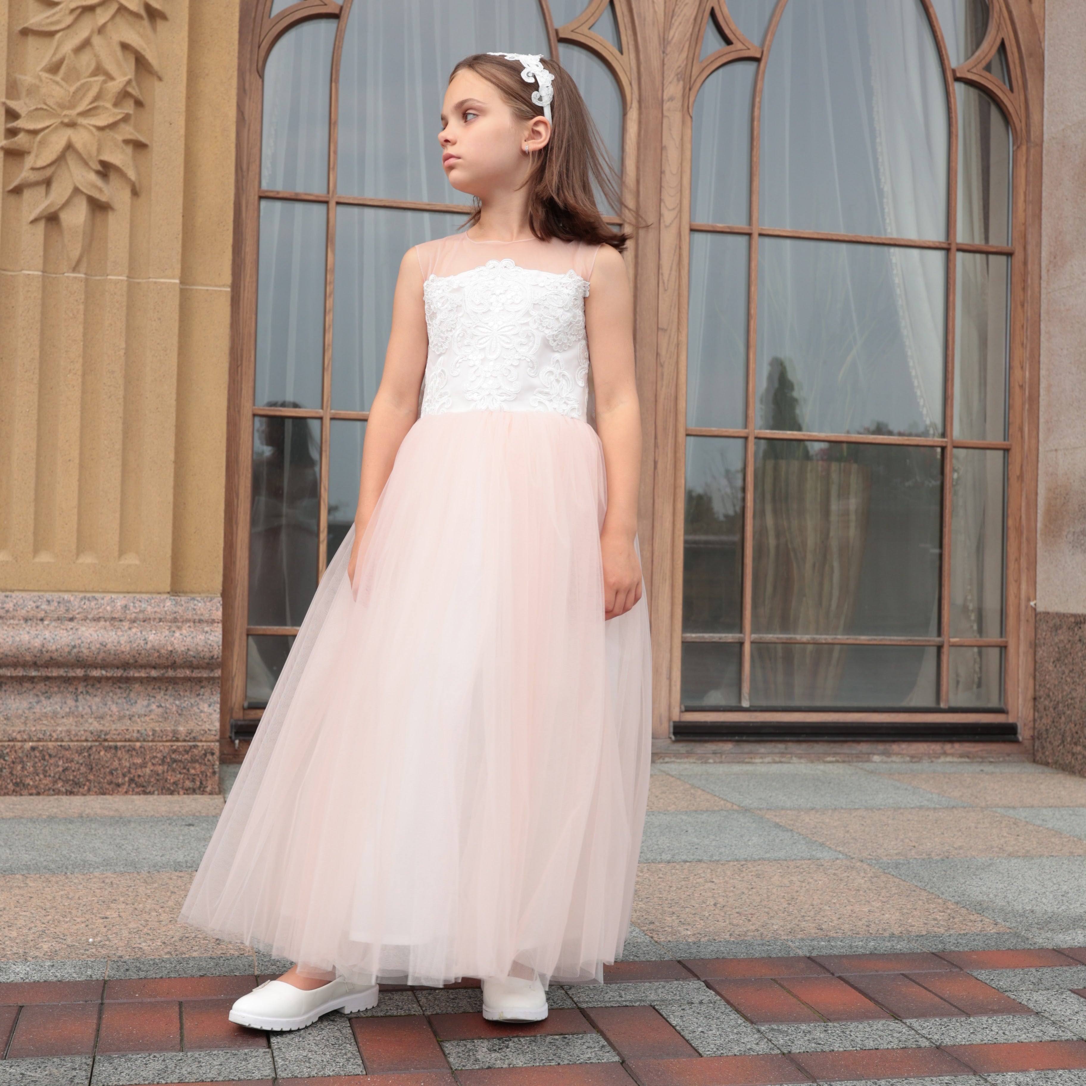 Young girl in a white lace top and pink tulle skirt standing in front of a decorative building entrance.