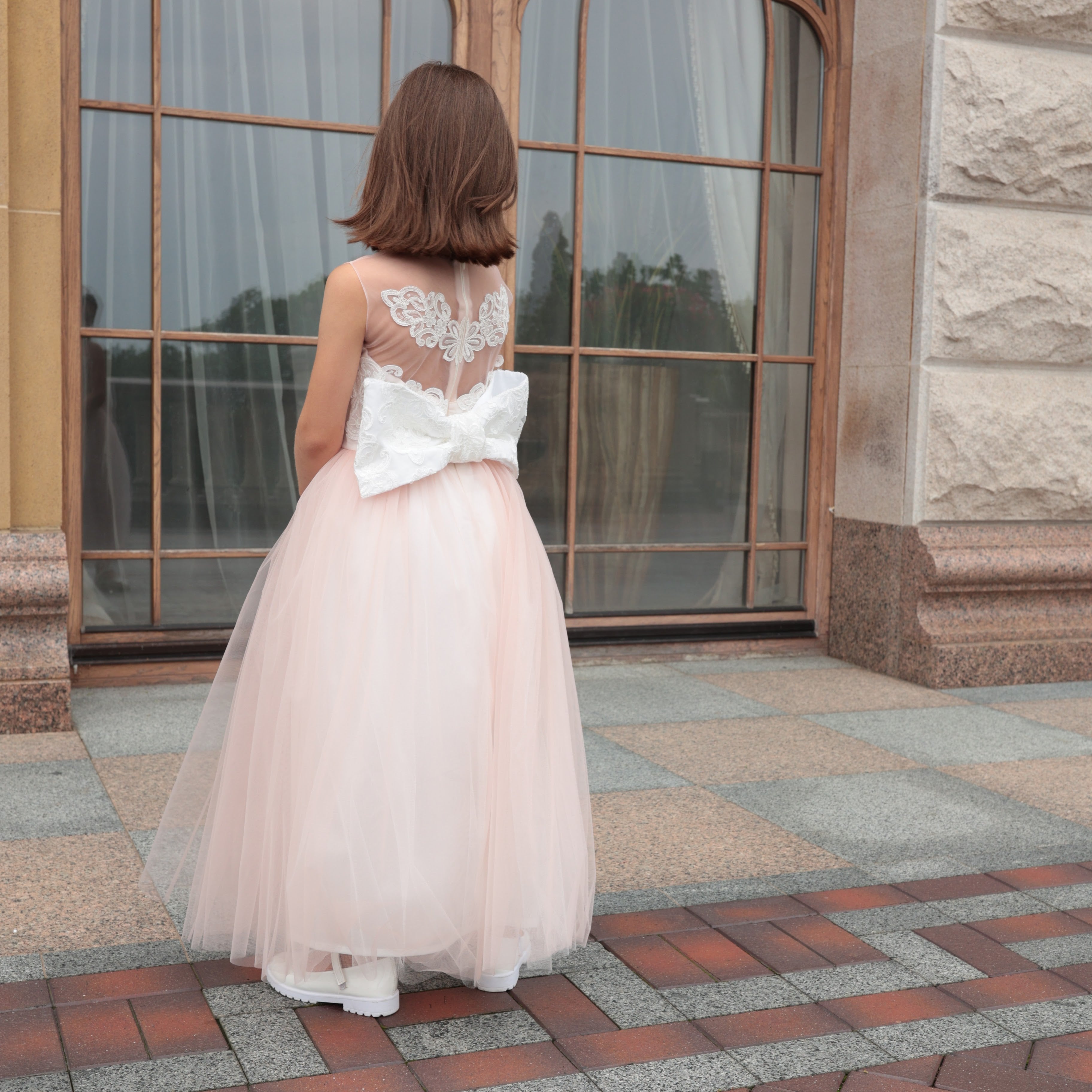 Woman in a pink dress with a large bow standing in front of a stone building.