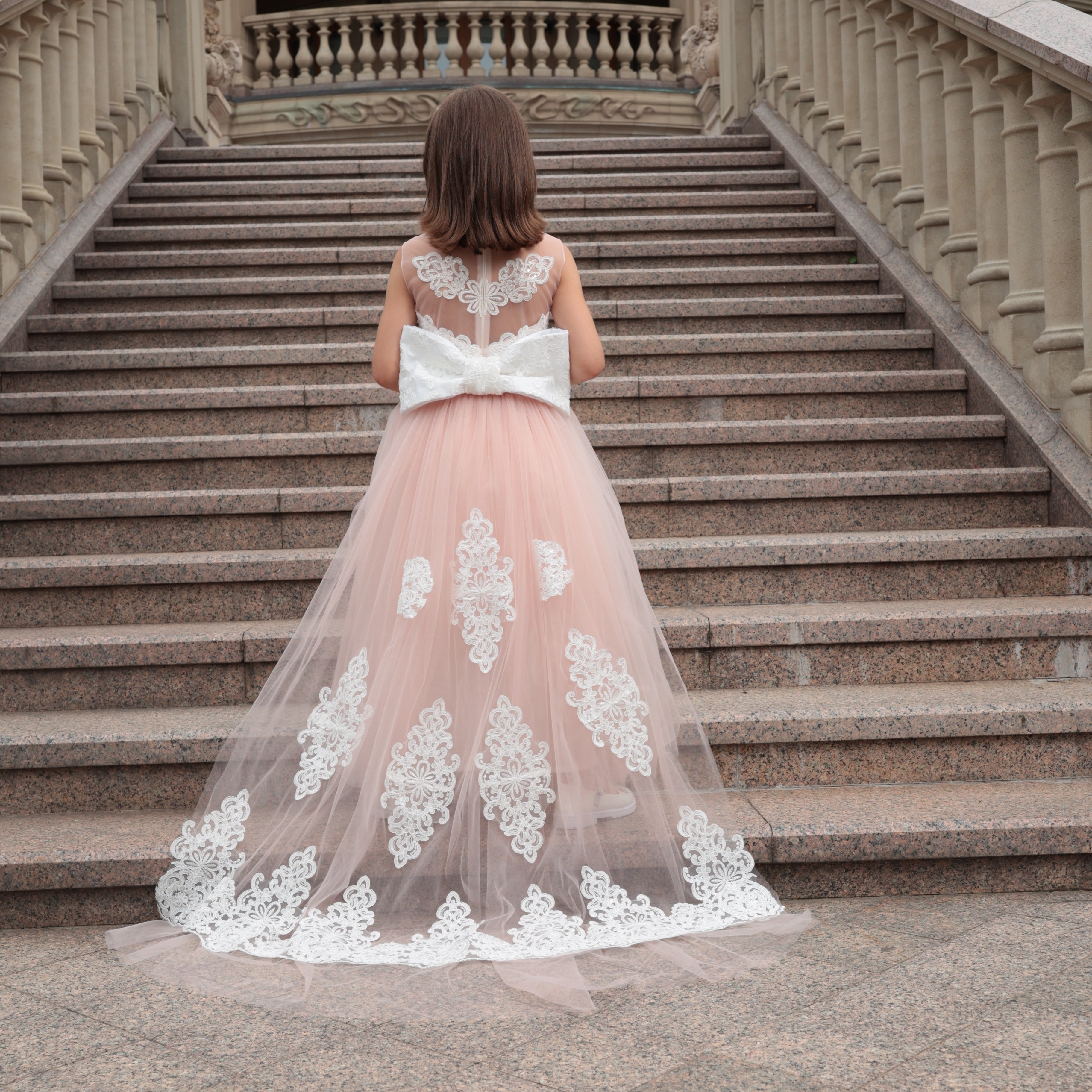 Woman in a pink and white lace dress walking up stone steps.