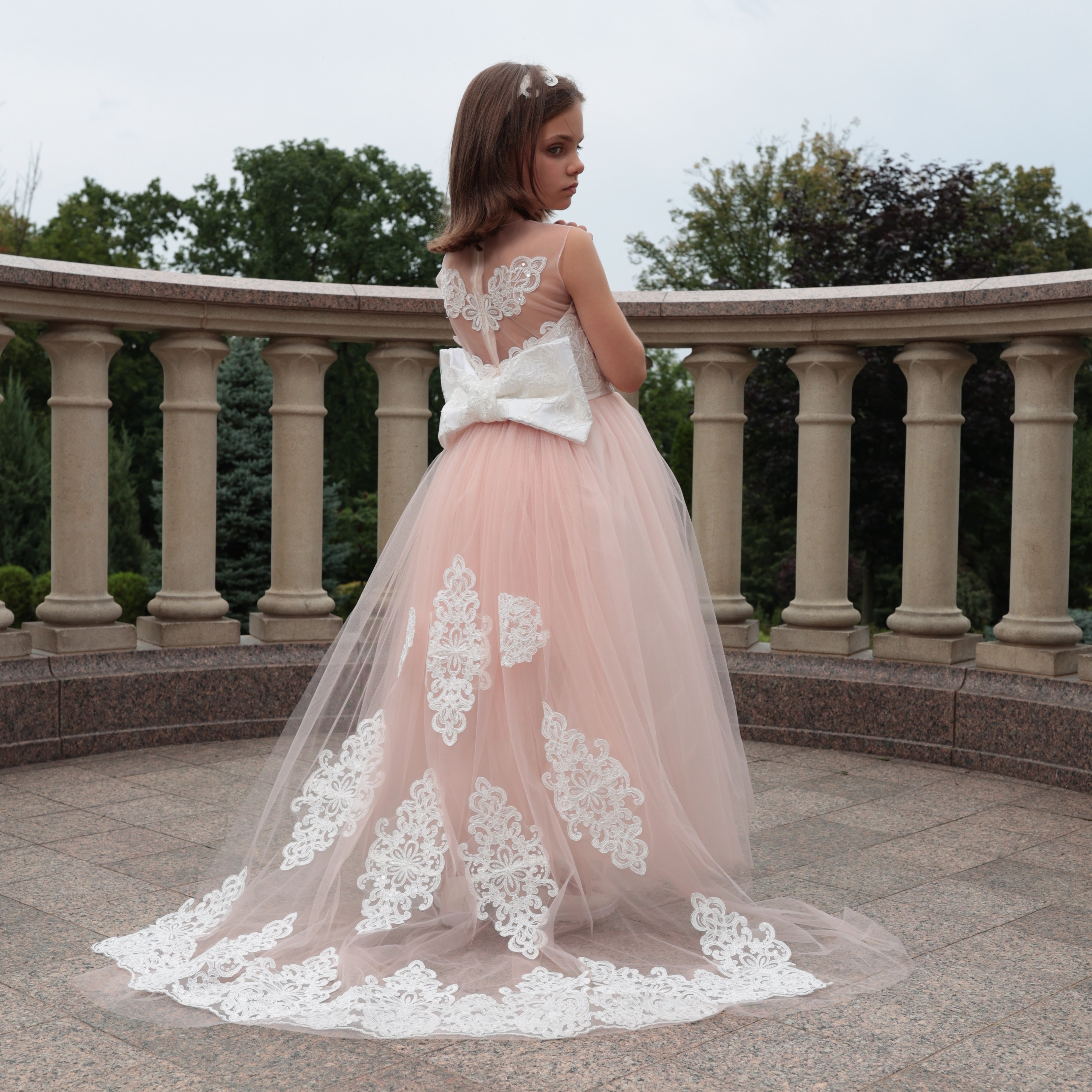Woman in a pink and white lace dress standing on a stone patio with columns.