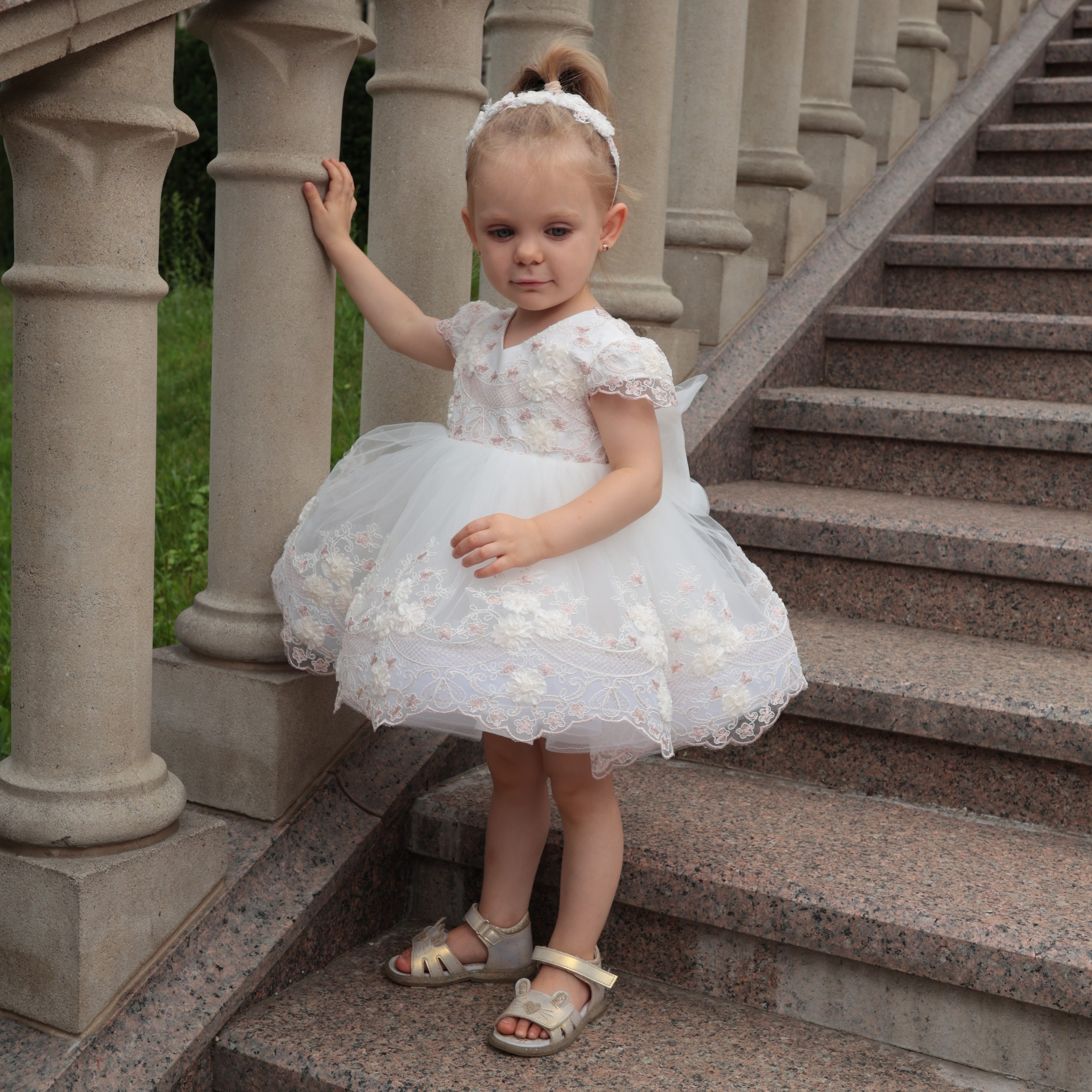 Young girl in a white dress standing on stone steps with columns in the background