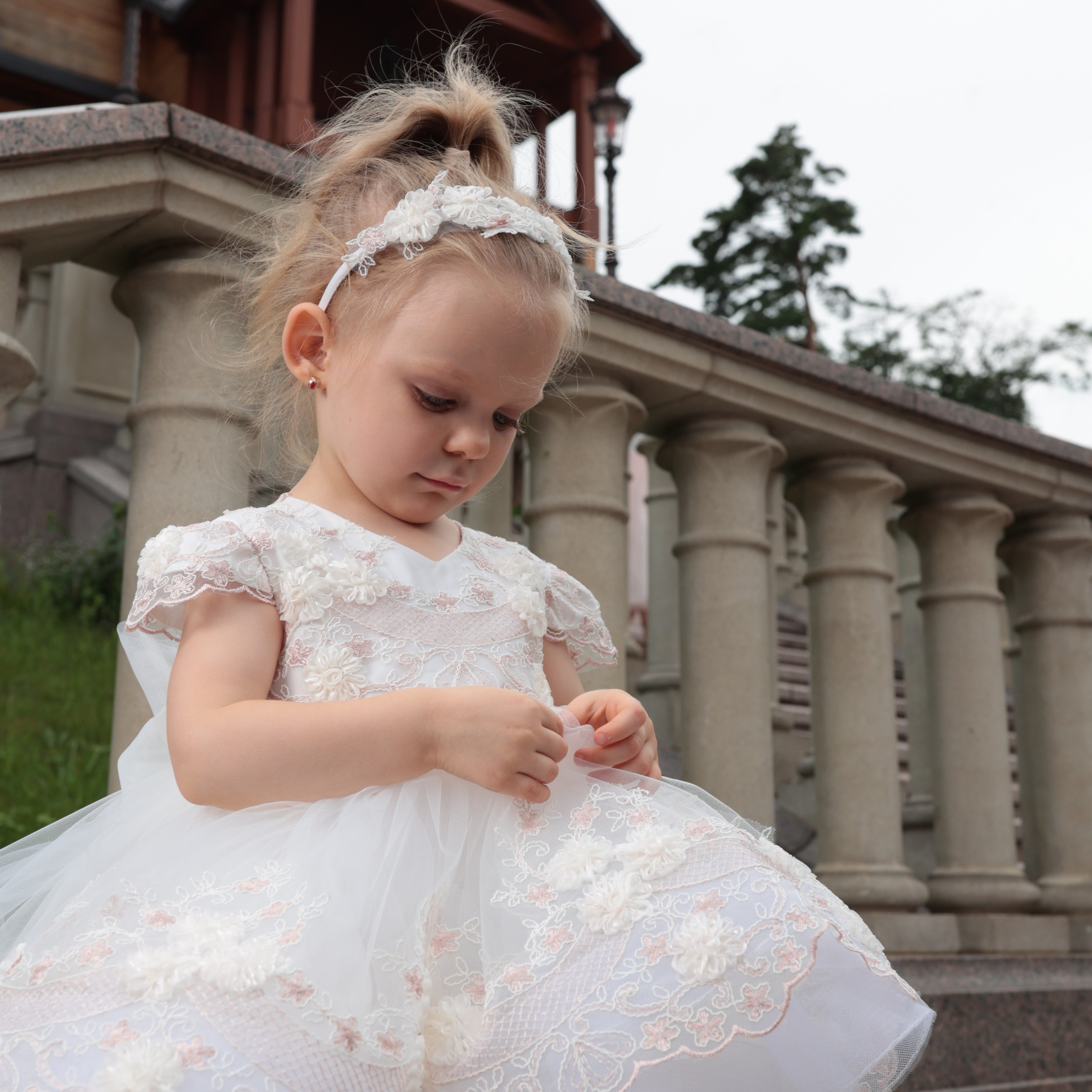 Young girl in a white dress standing outdoors with classical architecture in the background